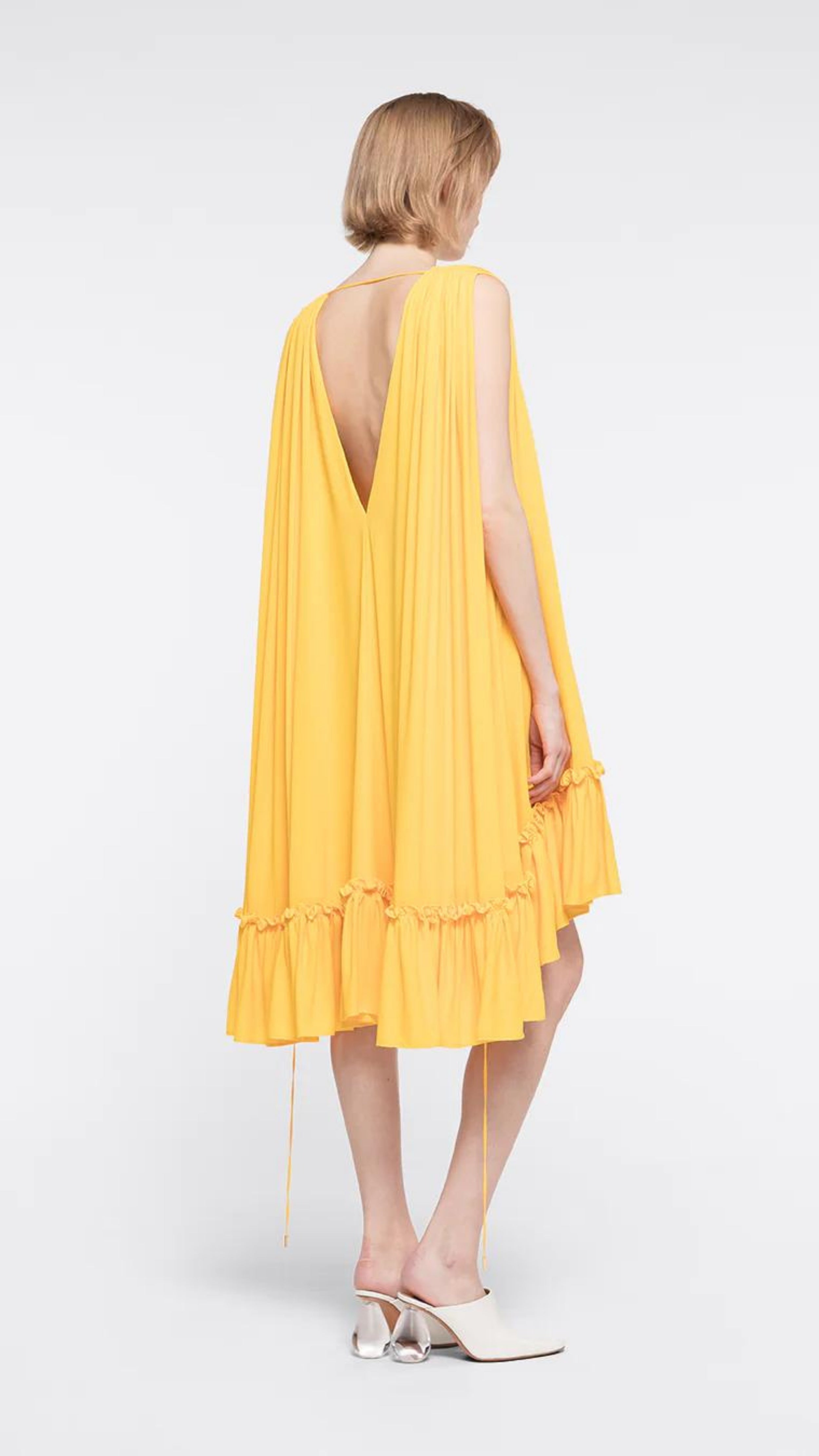 Az Factory Lutz Huelle Marilyn Dress. Bright yellow summer dress in trapeze style. With a v neck and volumnous a-line body and ruffled bottom. Shown on model facing back.