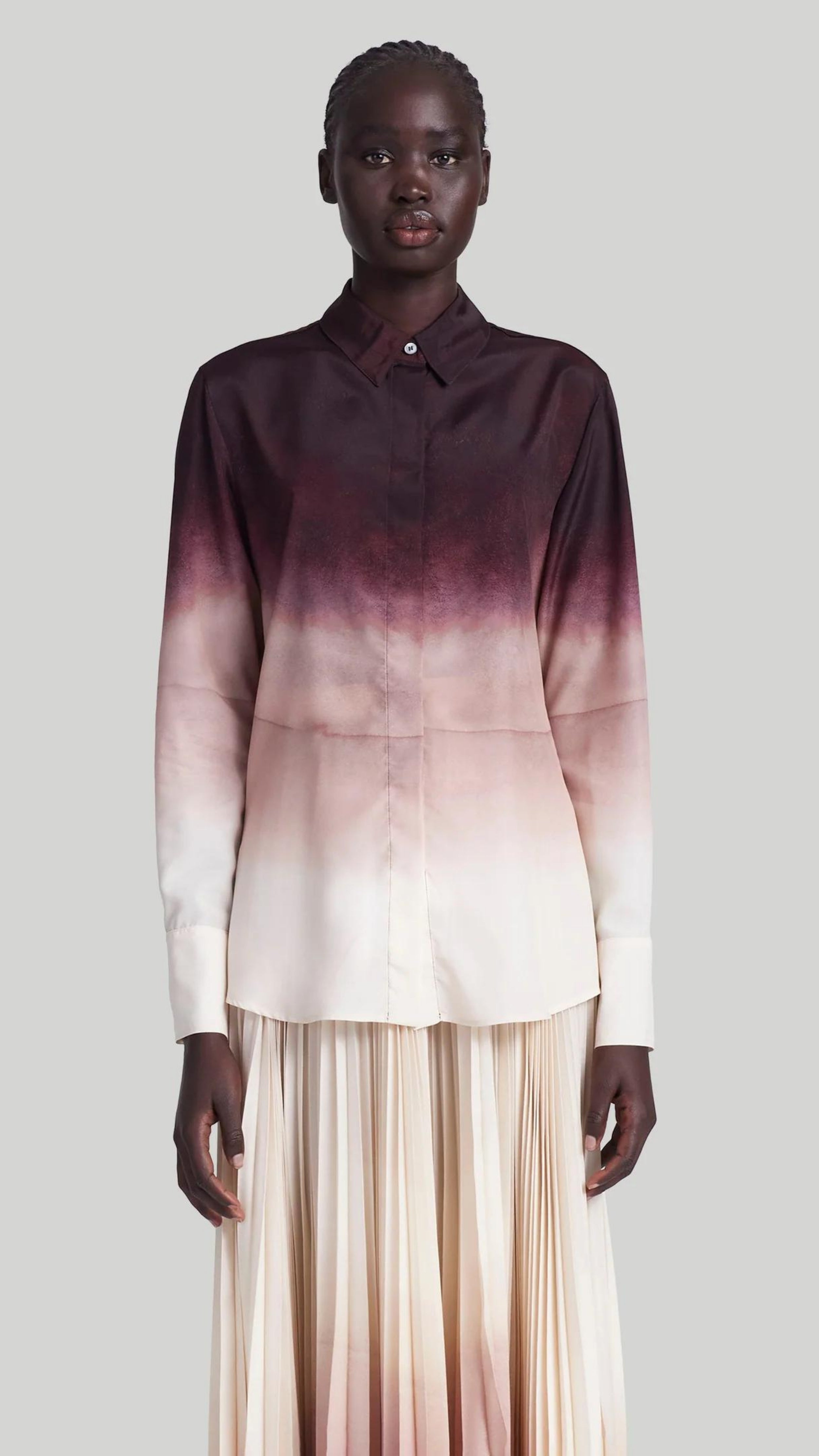 Altuzarra The Chika Top is crafted from Italian silk in an elegant cranberry to ivory dip dye ombre. The classic style button down shirt features a small point collar, concealed button front closure, and long cuffed sleeves. Shown on model facing front.