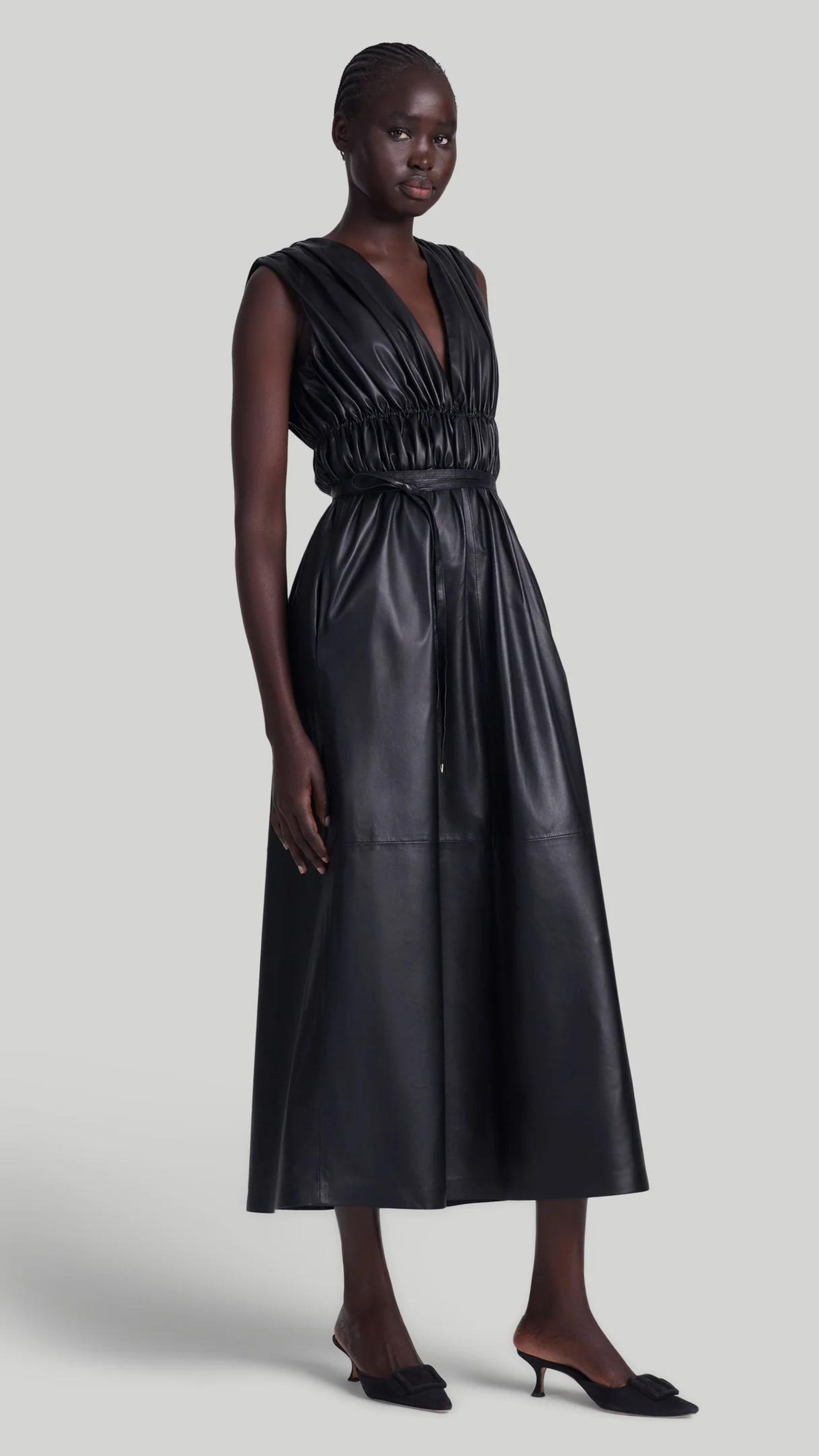 Altuzarra Fiona Dress, made from soft lamb leather. It features a maxi silhouette with a low V-neck, sleeveless, and ruching that folds at the waist with a thin leather belt. Shown on model facing front and to the side.