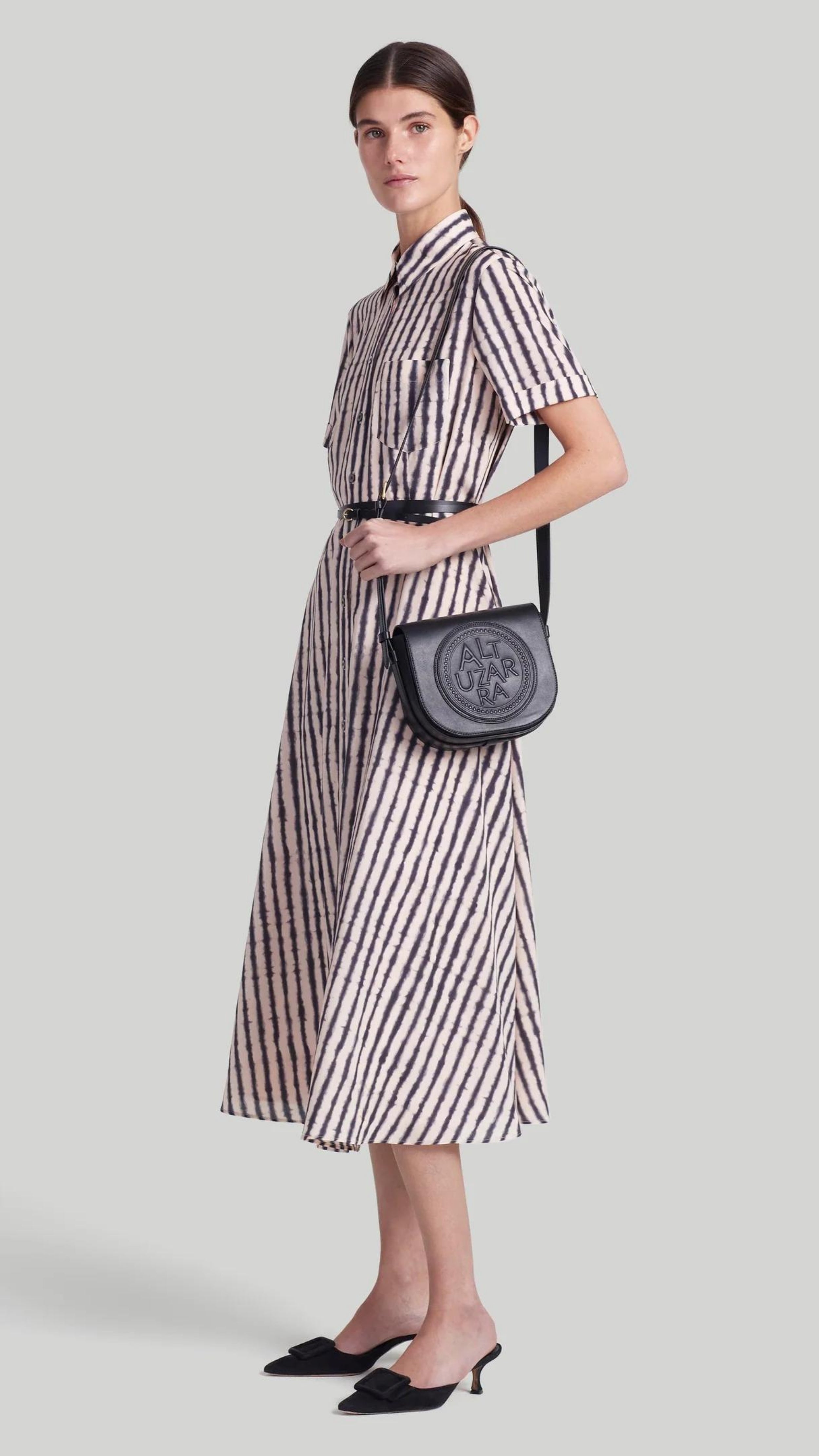 Altuzarra Kiera Dress The 'Kiera' dress is designed with a small point collar, short sleeves and a flattering A-line skirt. It is detailed with a slim leather waist belt and features a black and white stripe pattern and a front breast pocket. Shown on model facing front and side.