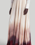 Altuzarra Sif Skirt A tailored maxi skirt with a straight high waistband and a voluminous pleated skirt. Made from 100% Italian silk it is dip dyed in an ombre of in cranberry to ivory coloring. On model facing front and side.