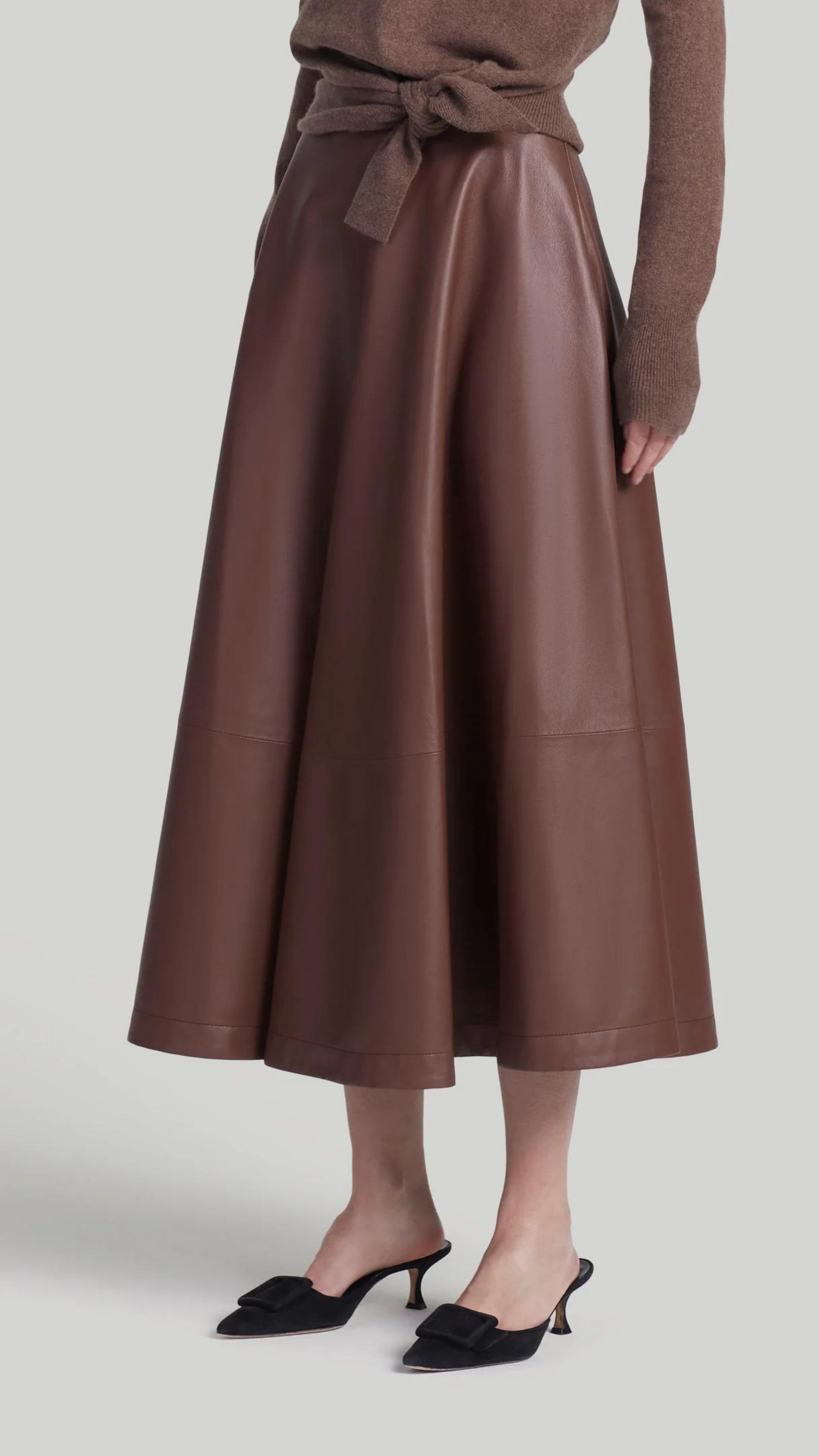 Altuzarra Varda Skirt Made from soft, subtle brown lamb leather, it has an A-line skirt. Midi-length SS24 runway piece. The skirt hem falls to just below the knee. Shown on model facing front and side.