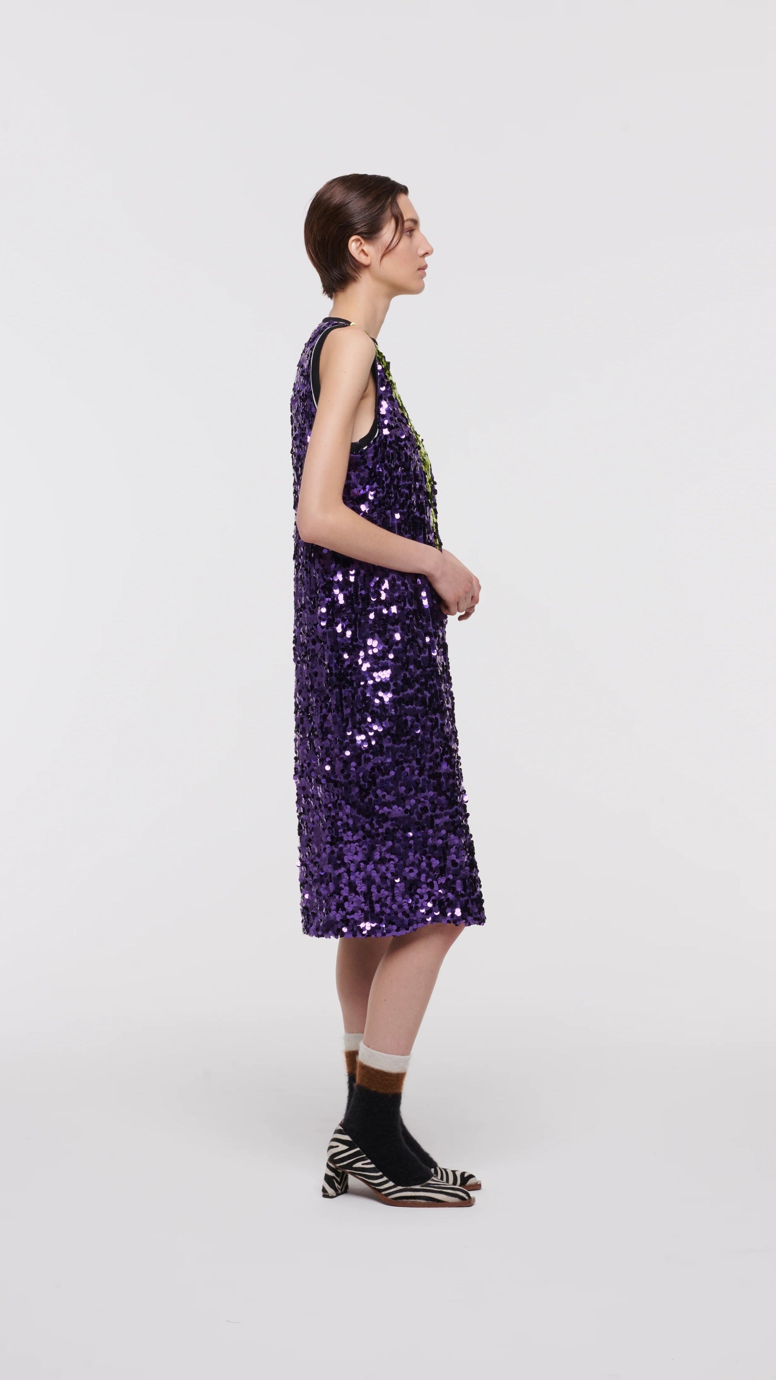 Plan C Color Block Sequin Dress. Sleeveless racer back style midi length dress in purple and lime green. Trimmed in black at the neckline and arms. The green sequins form a v shape in the front. Shown on model facing side.