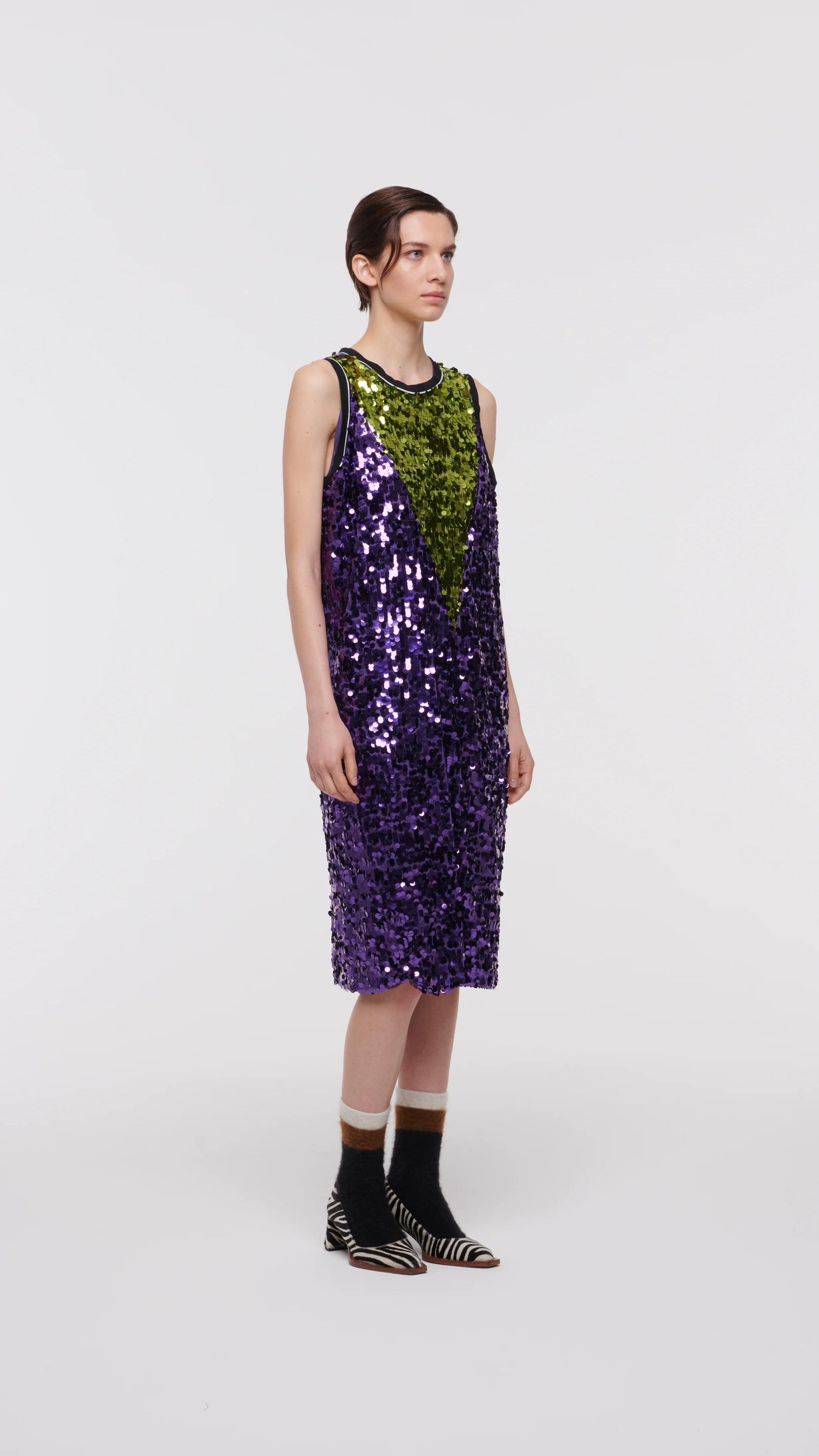 Plan C Color Block Sequin Dress. Sleeveless racer back style midi length dress in purple and lime green. Trimmed in black at the neckline and arms. The green sequins form a v shape in the front. Shown on model facing forward.