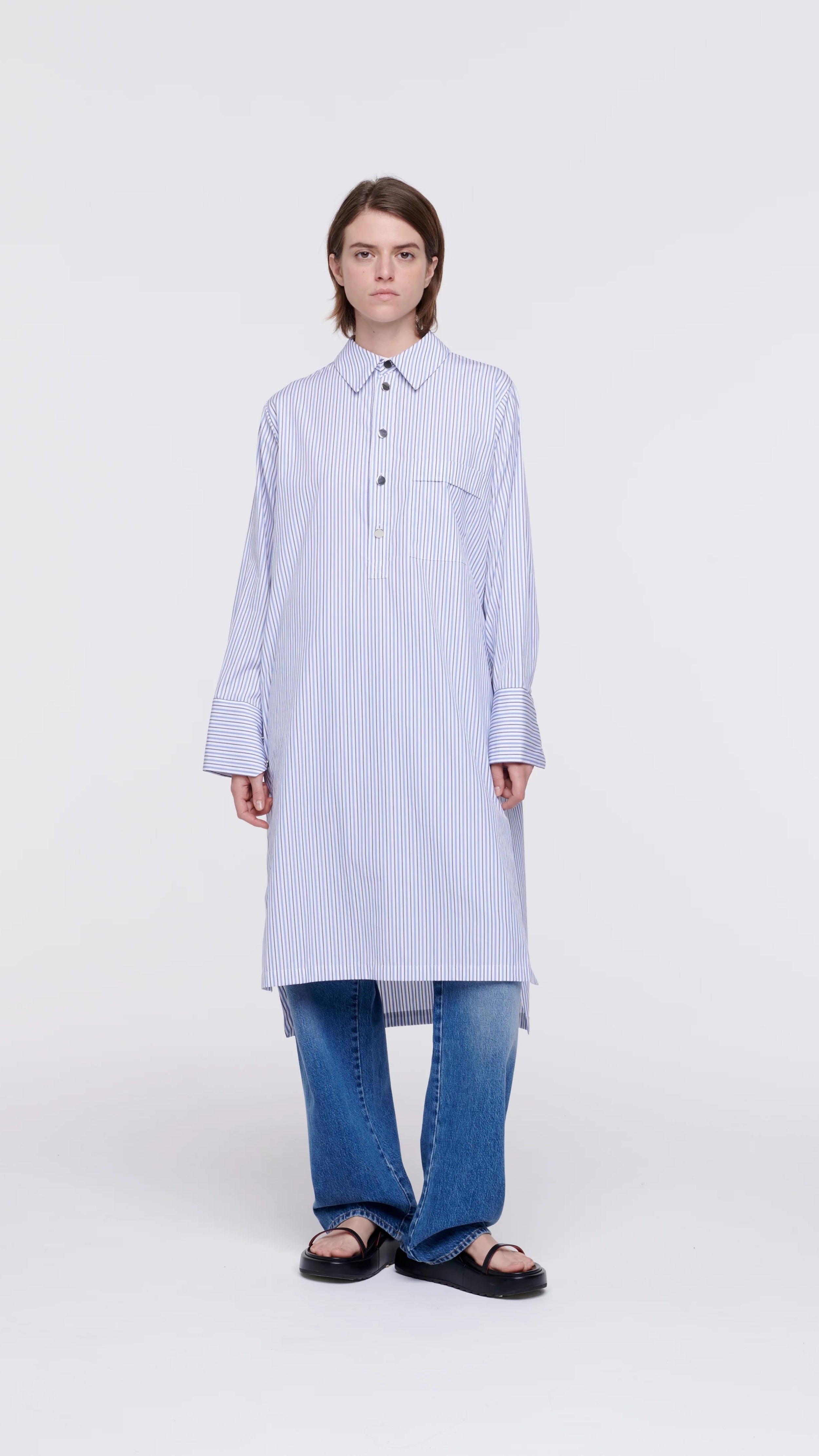 Plan C Striped Cotton Poplin Shirt Dress Classic yet modern shirt dress made from soft cotton poplin in pale blue and white stripes. It has three silver buttons, a collared neckline, long cuffs, and a breast pocket. It's designed with a relaxed fit and side pockets. Shown on model facing front