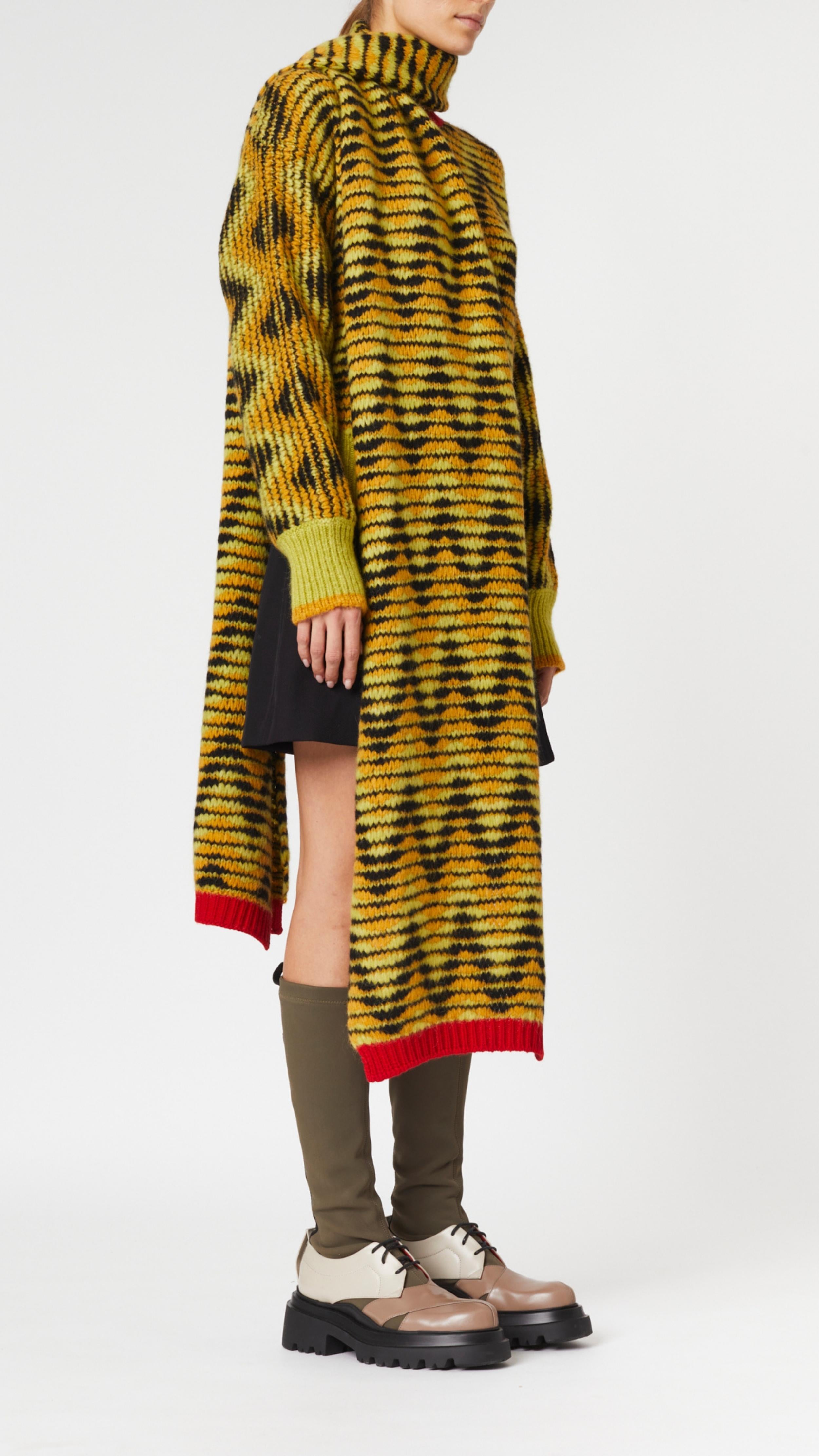 Plan C Jacquard Knit Oversize Scarf in pistachio, black and ochre colored chevron V pattern. Pop of red at the trim. Super oversized made from soft alpaca and wool blend. Photo shown on model wearing it with matching Long Sleeve Jacquard Knit Sweate 