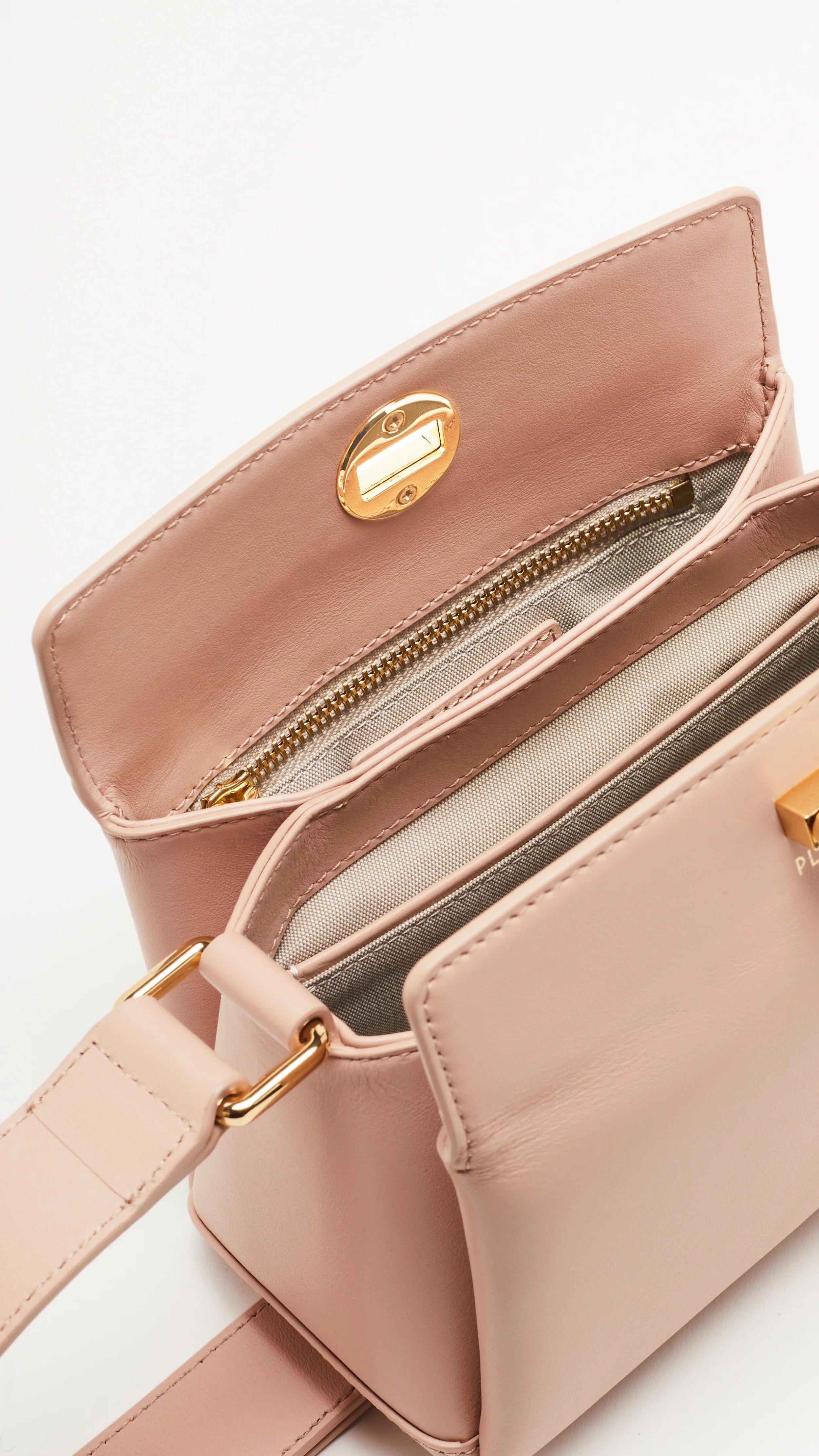 Plan C The Mini Folded Bag in Sand Pink. Luxury handbag crafted in Italy from soft calfskin with an adjustable leather shoulder strap. This purse has a gold-toned turnstile top closure and offers three compartments, one flat zipped and one snap buttoned pocket. Photo shows the interior detail.