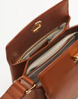 Plan C The Mini Folded Bag in Toasted Brown. Luxury handbag crafted in Italy from soft calfskin with an adjustable leather shoulder strap. This purse has a gold-toned turnstile top closure and offers three compartments, one flat zipped and one snap buttoned pocket.  Photo shows interior details.