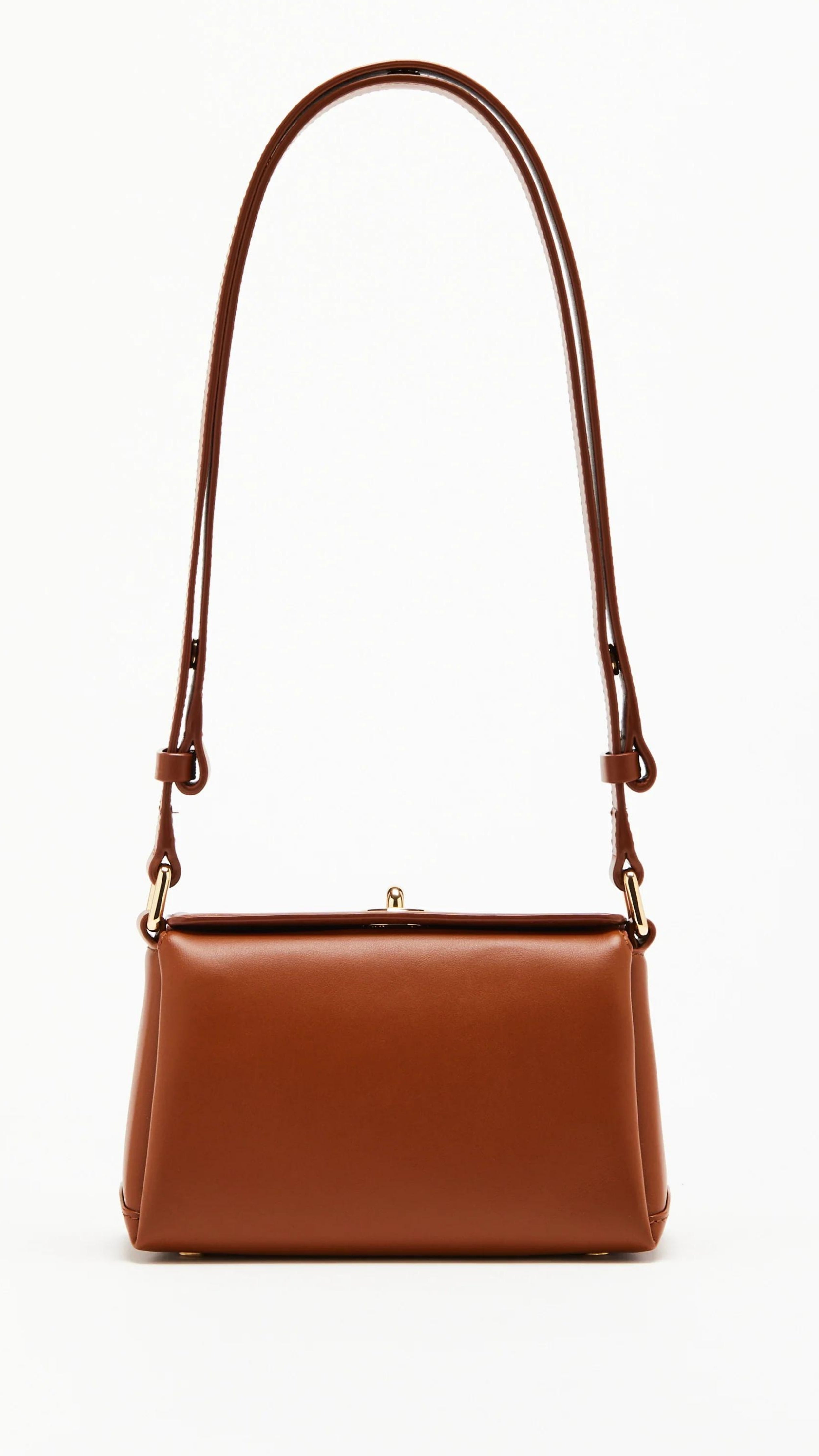 Plan C The Mini Folded Bag in Toasted Brown. Luxury handbag crafted in Italy from soft calfskin with an adjustable leather shoulder strap. This purse has a gold-toned turnstile top closure and offers three compartments, one flat zipped and one snap buttoned pocket.  Photo shown from the front view with the adjustable shoulder strap.