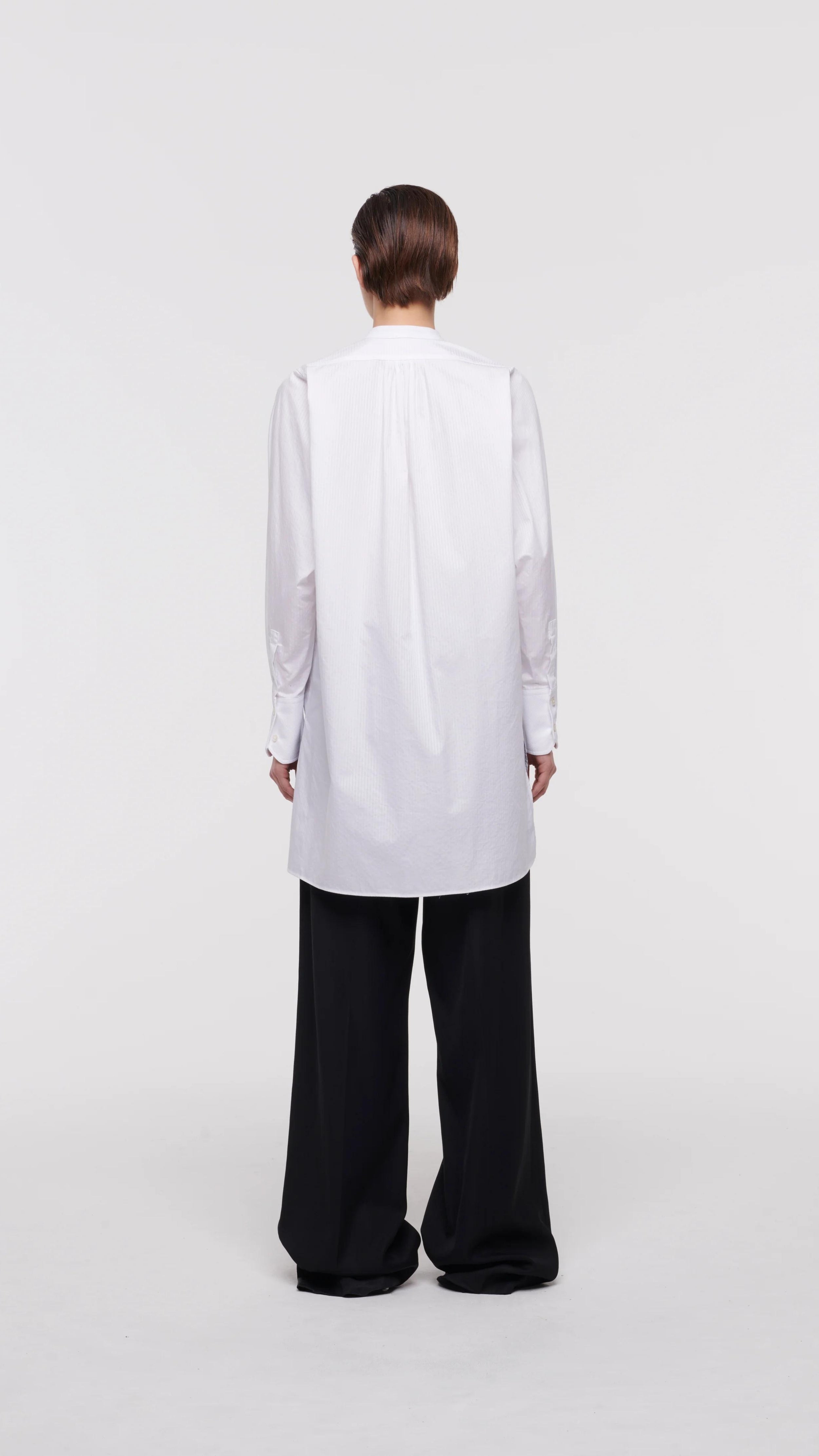 Plan C White Sartorial Poplin Shirt. Classic with a twist long white poplin blouse with front buttons. An added black ribbon detail in the front. Oversized cuffs at the long sleeves. Product photo shown from the back.