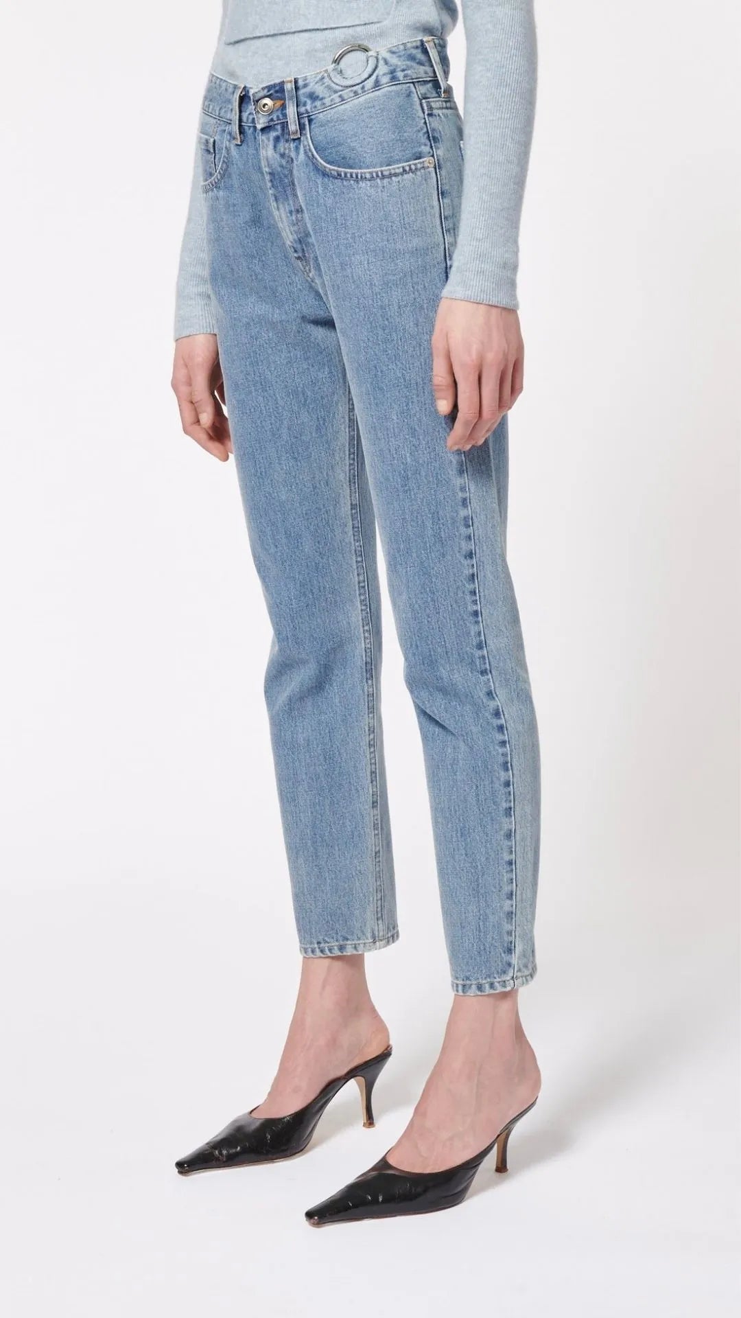 Boyarovskaya Slim Ring Jean. Light color stone denim with a slightly tapered leg and falls to just above the ankle. Zipper closure with silver ring detail on the front right. Product shown on model facing side.