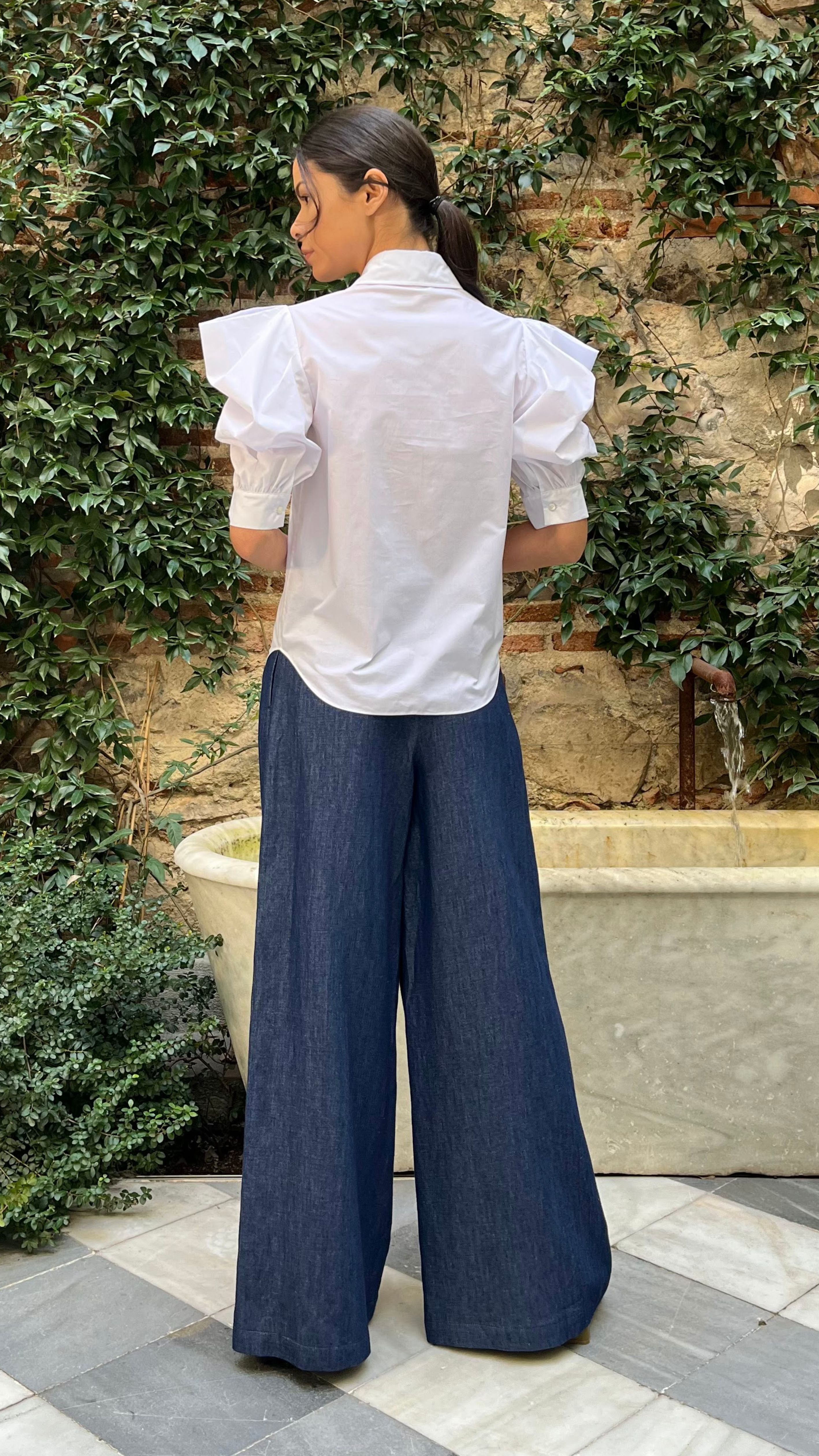 Rochas Paris Cotton Poplin Short Sleeved Shirt. A button up blouse in lightweight cotton it has two front pockets and puffed sleeves. Photo shown on model also wearing Rochas wide leg denim trousers from the back view