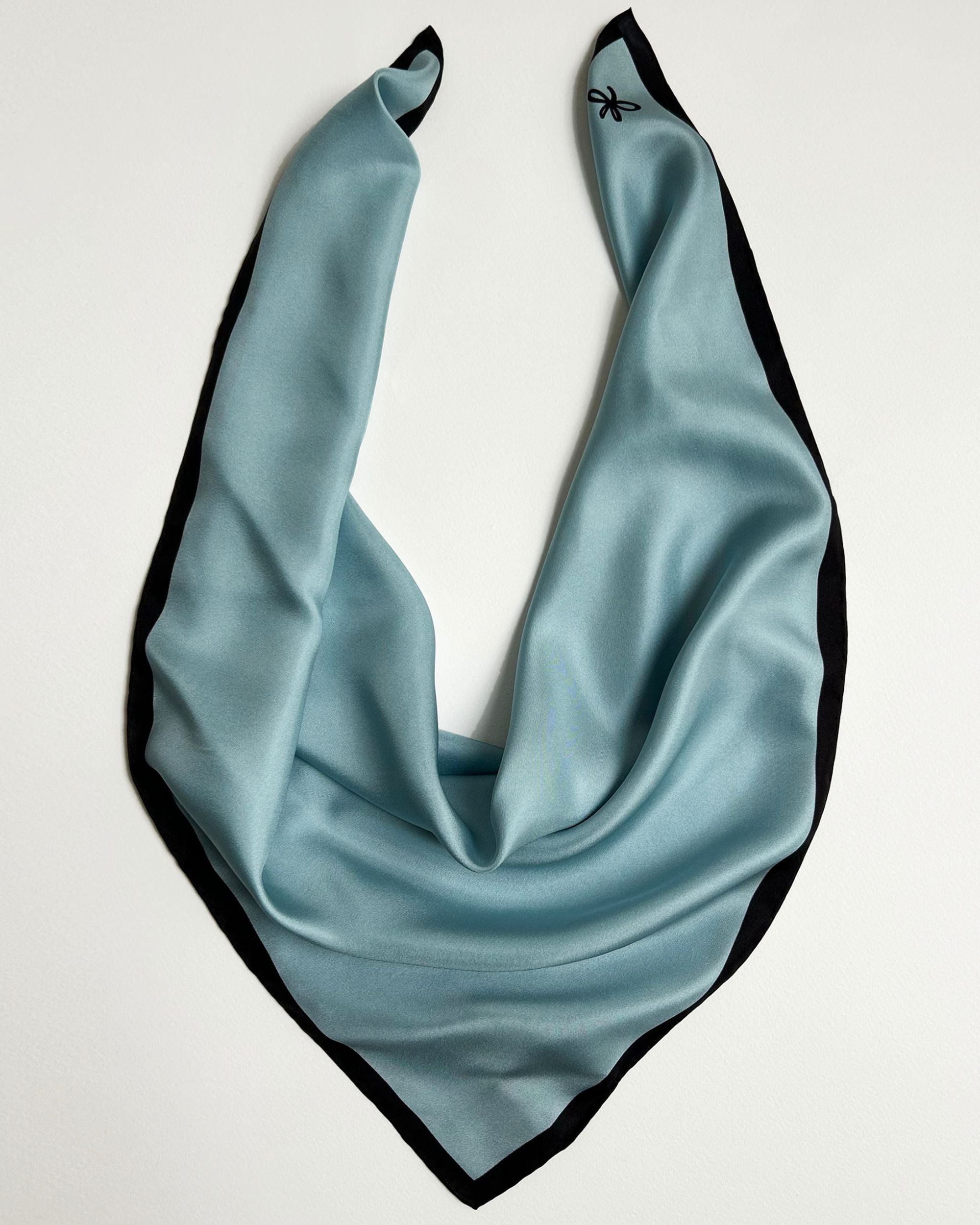 Square light blue silk scarf laid flat with black border