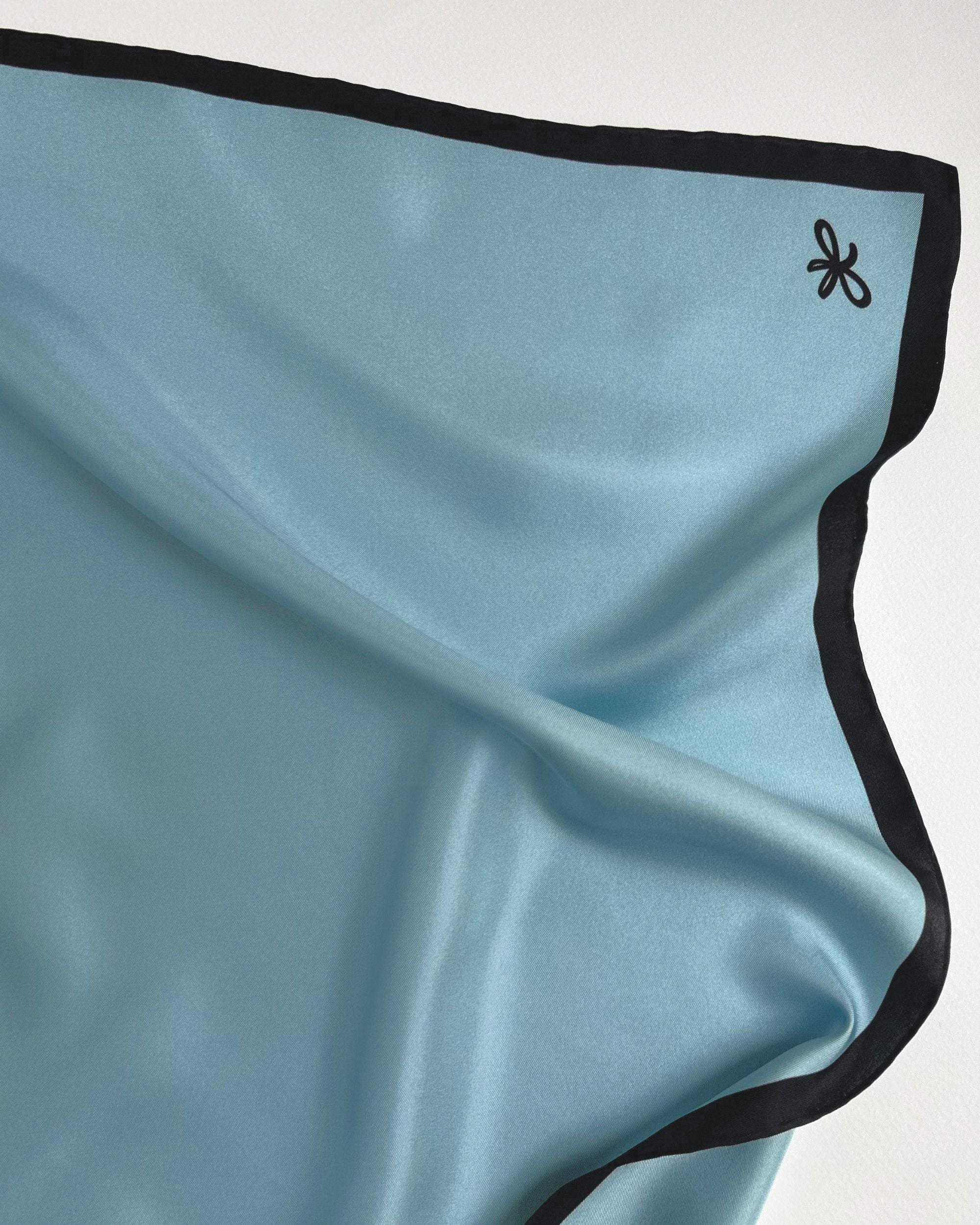 Close-up of light blue silk scarf with black border and logo
