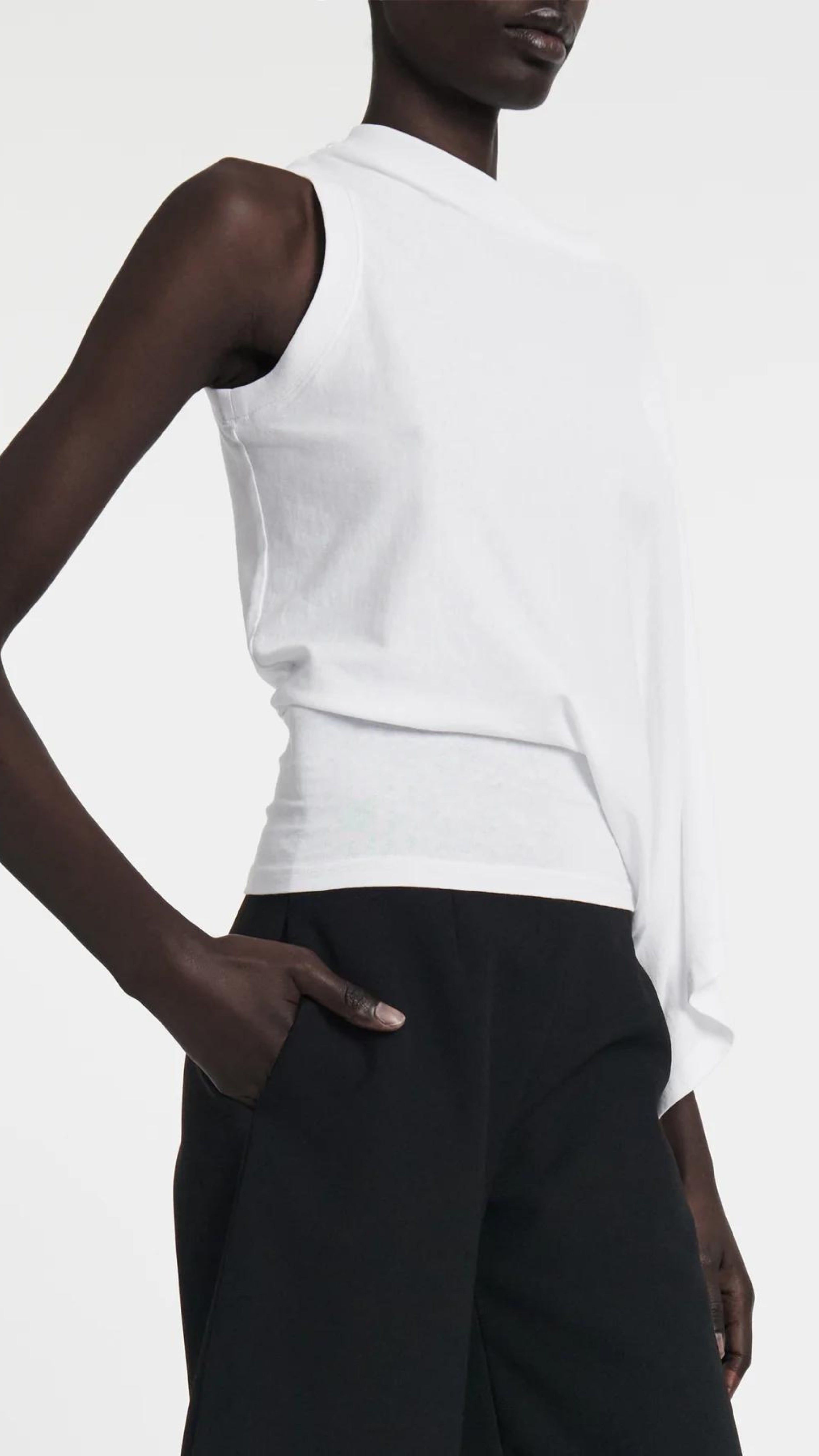 A.W.A.K.E. Mode Asymmetrical One Sleeve T-Shirt in white cotton. Sleeveless on one side and with an exaggerated sleeve on the other. Rounded t-shirt neckline that is slightly off the shoulder. The waist is fitted so the shirt drapes beautifully. Shown on model facing side
