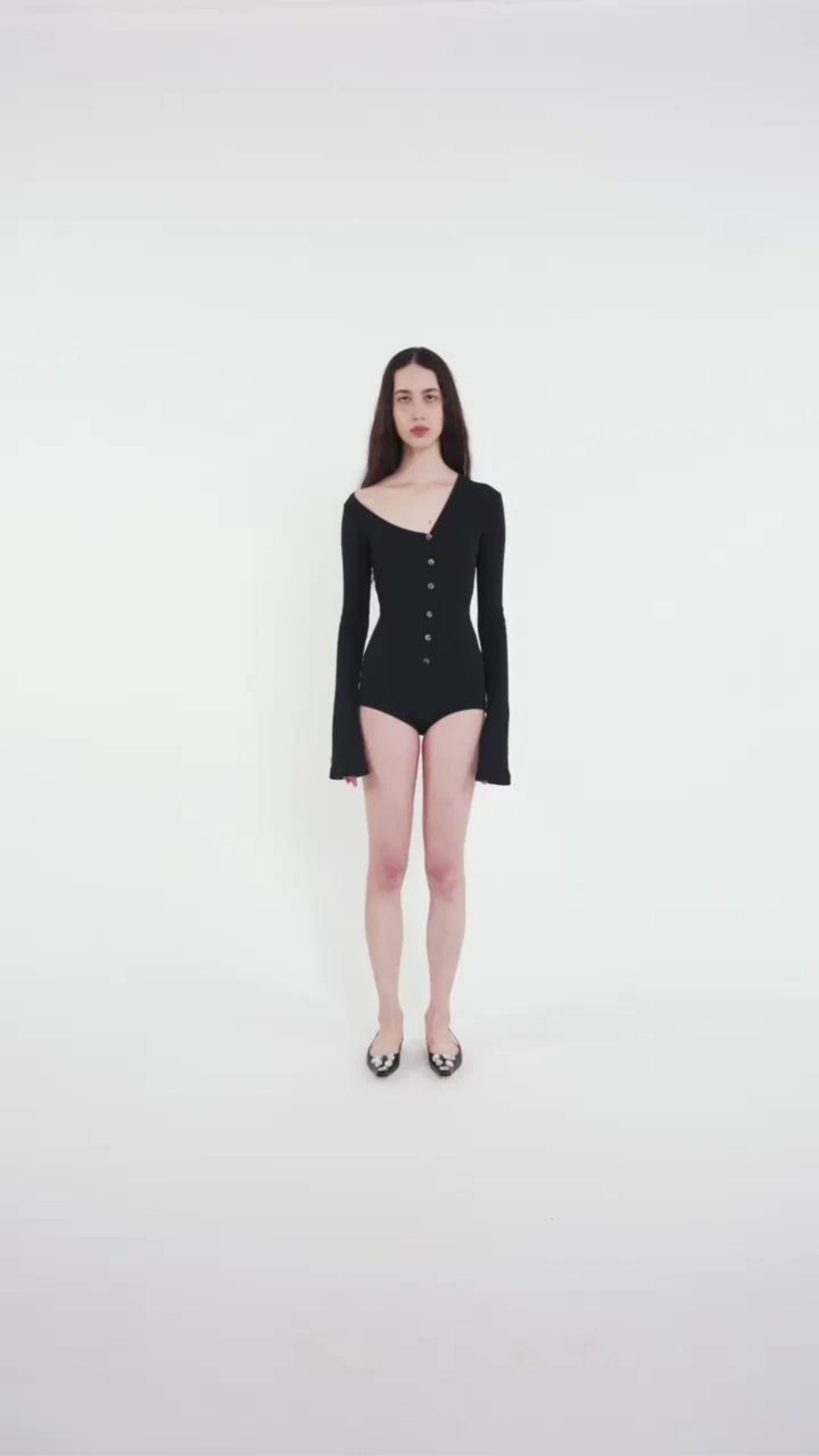 AWAKE Mode Body Suit with Asymmetrical Collar in Black. 100% Cotton top with an asymmetrical collar. Slightly off shoulder on one side. Buttons up the front and extra long sleeves. Shown on model facing front.