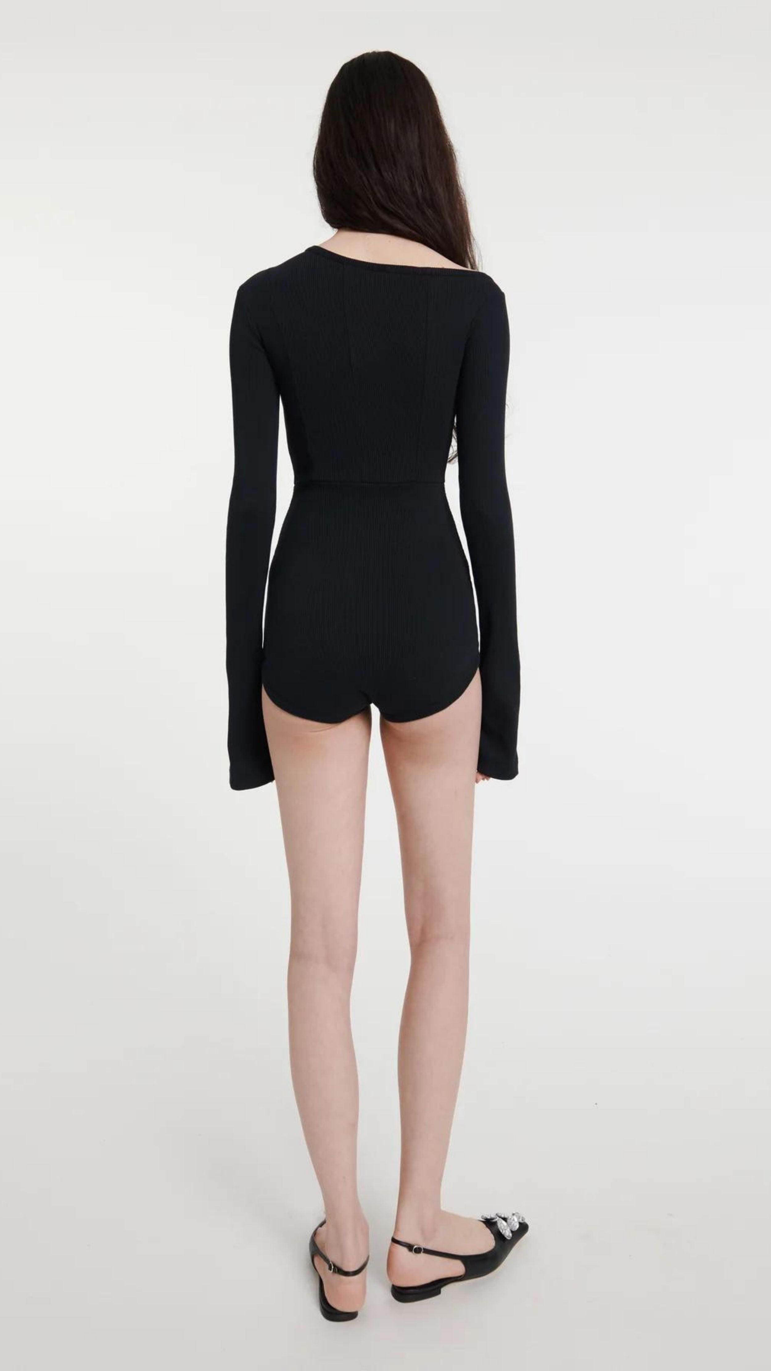 AWAKE Mode Body Suit with Asymmetrical Collar in Black. 100% Cotton top with an asymmetrical collar. Slightly off shoulder on one side. Buttons up the front and extra long sleeves. Shown on model facing back.