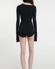 AWAKE Mode Body Suit with Asymmetrical Collar in Black. 100% Cotton top with an asymmetrical collar. Slightly off shoulder on one side. Buttons up the front and extra long sleeves. Shown on model facing back.