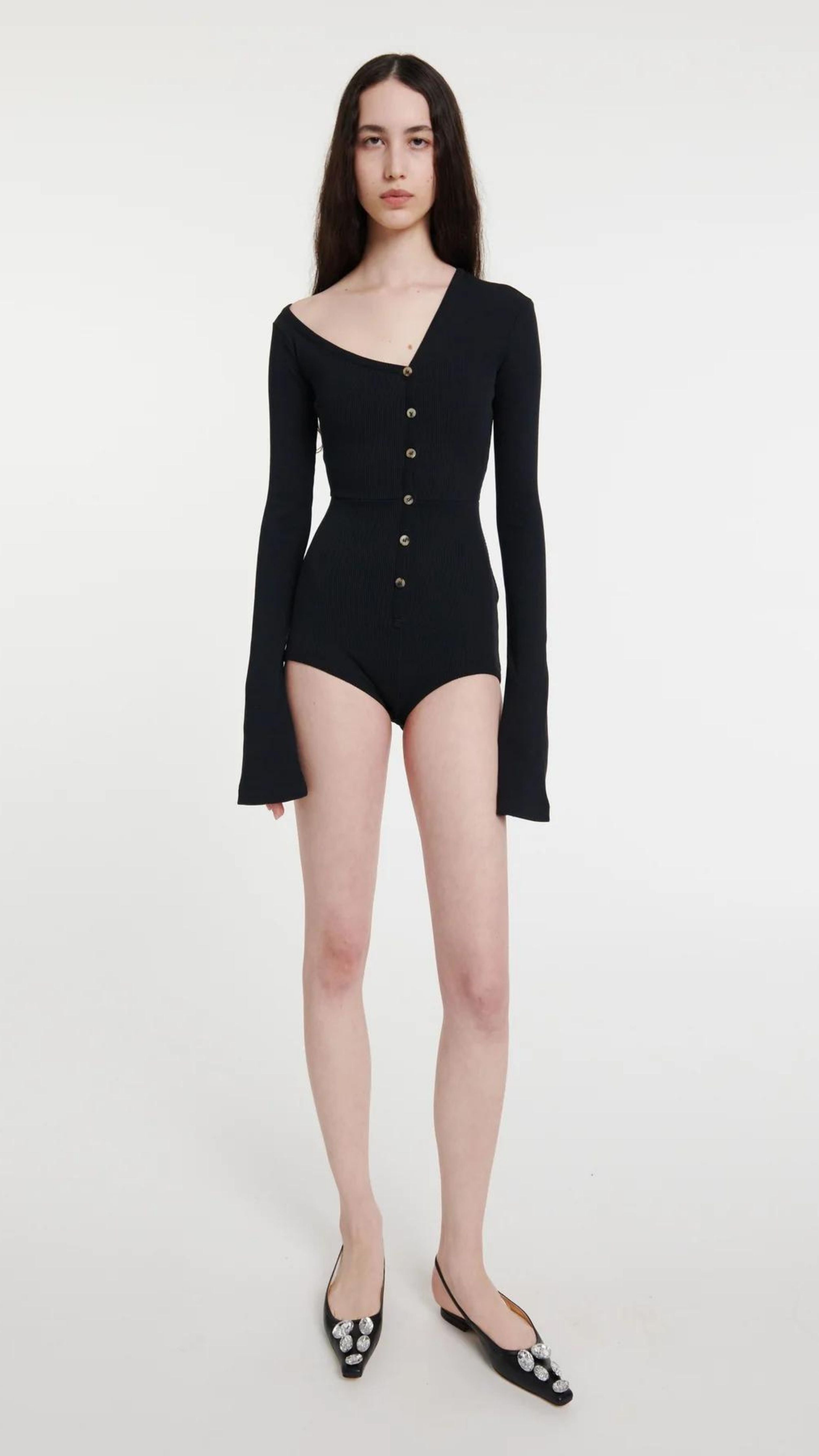 AWAKE Mode Body Suit with Asymmetrical Collar in Black. 100% Cotton top with an asymmetrical collar. Slightly off shoulder on one side. Buttons up the front and extra long sleeves. Shown on model facing front.