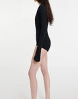 AWAKE Mode Body Suit with Asymmetrical Collar in Black. 100% Cotton top with an asymmetrical collar. Slightly off shoulder on one side. Buttons up the front and extra long sleeves. Shown on model facing side.