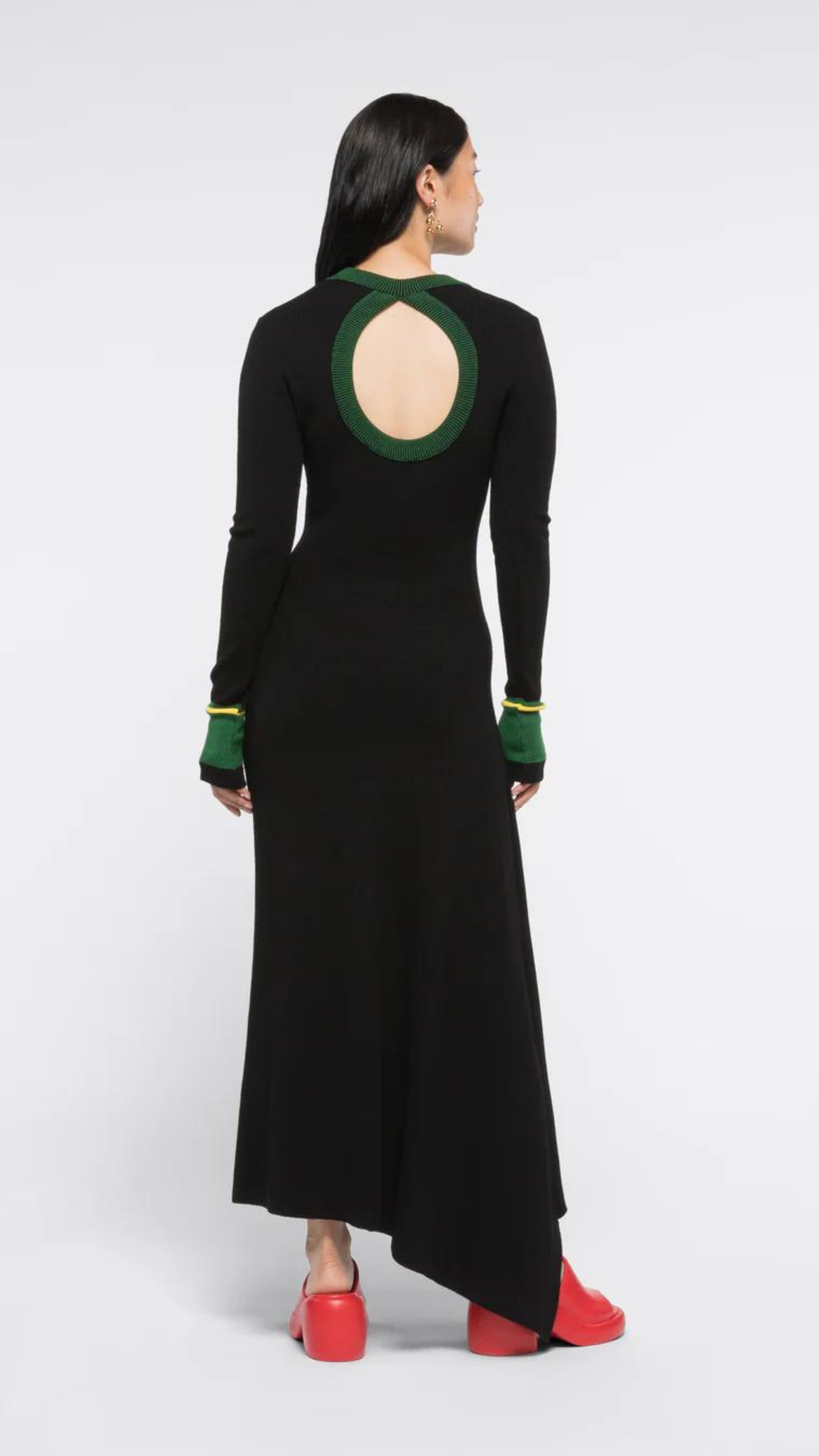 AZ Factory Colville Molly Molloy and Lucina Chambers Back Keyhole Asymmetrical Dress. Knit dress in black with a key hole cut out in the back. The neckline and the cuffs are rimmed in green and yellow. Asymmetrical long hem. Shown on model facing back.