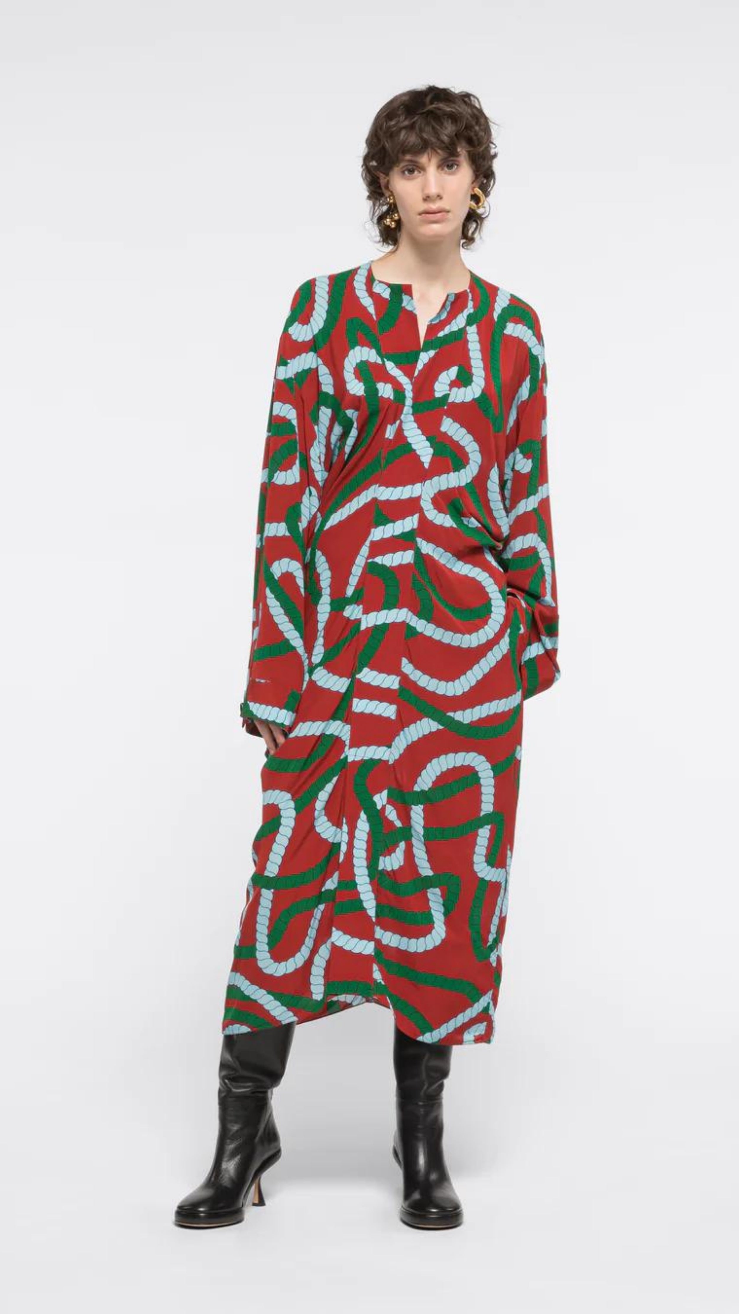 AZ Factory Colville Molly Molloy Lucinda Chambers, Printed Draped Midi Dress. Midi dress with long sleeves and a v cut neckline. It's a rust red with intertwining  rope pattern in green and sky blue. Shown on model facing front.