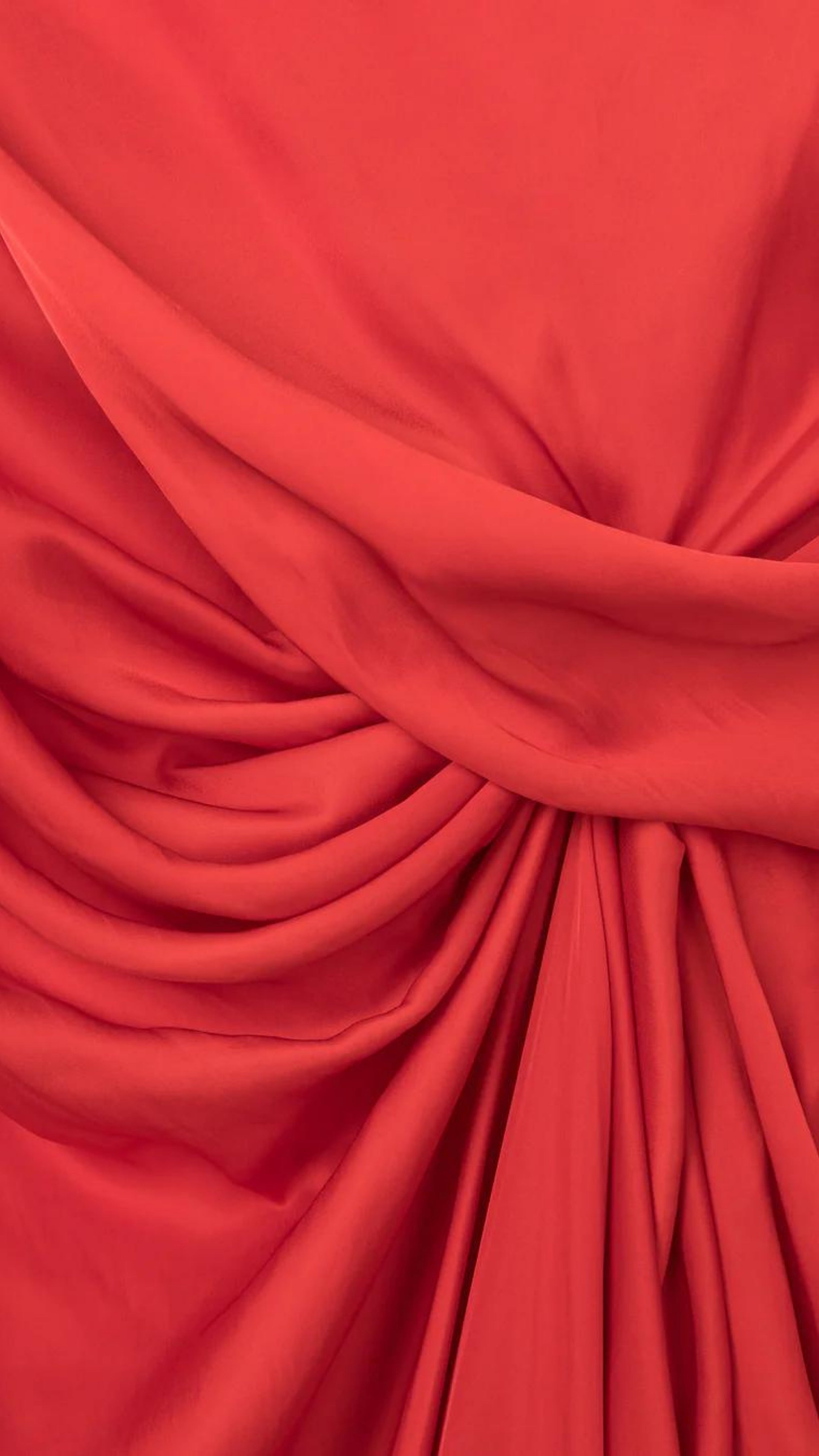 AZ Factory Colville Molly Molloy Lucinda Chambers, Sleeveless Draped Dress in Red An elegant red formal dress with a silhouette defined by a straight neckline and asymmetrical hemline. The waistline has detailed draping and the front leg as a slit. Close up of fabric and color.