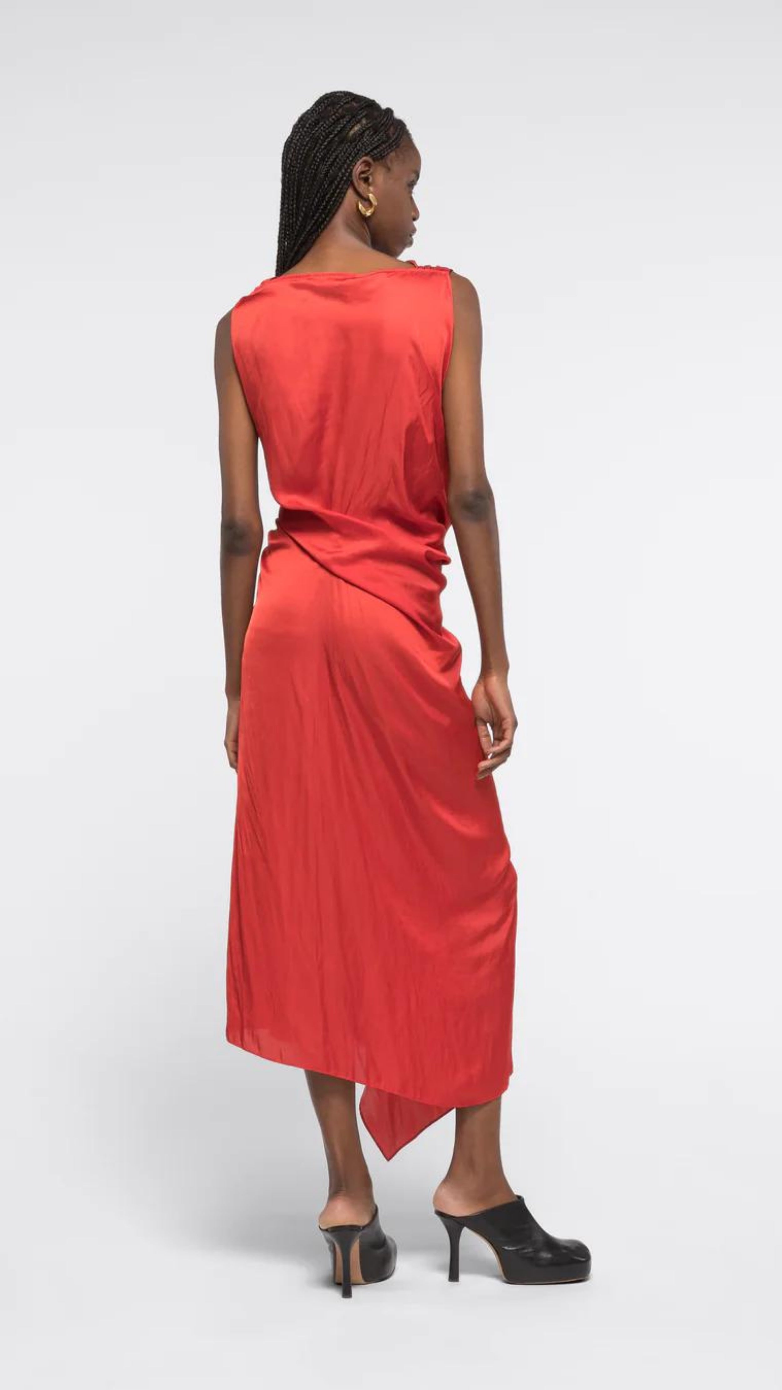 AZ Factory Colville Molly Molloy Lucinda Chambers, Sleeveless Draped Dress in Red An elegant red formal dress with a silhouette defined by a straight neckline and asymmetrical hemline. The waistline has detailed draping and the front leg as a slit. Shown on model from back.