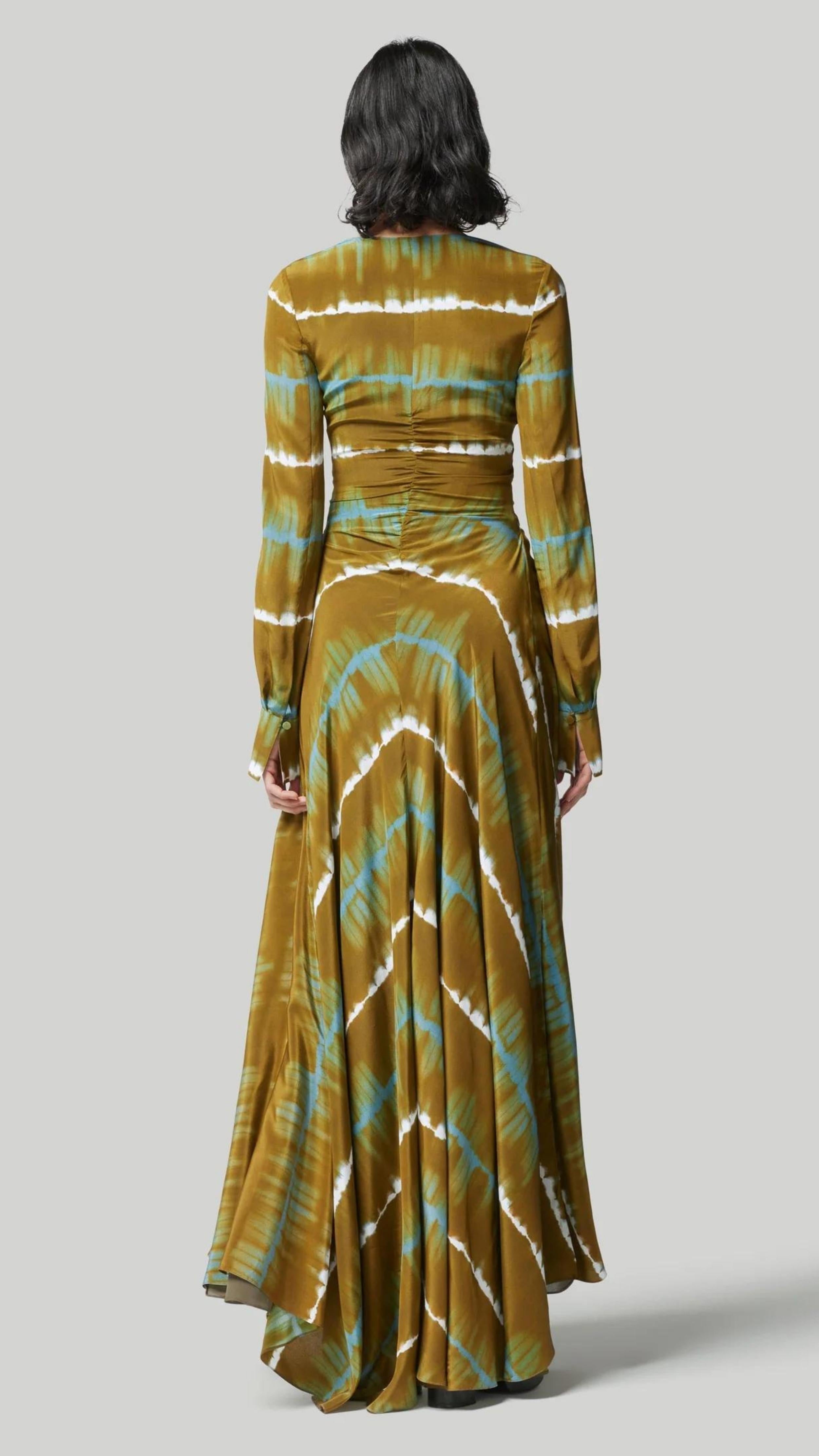 Altruzarra, Helenos Dress. 100% silk and shibori dyed in beautiful olive green and ecru pattern with a highlight pop of blue/green. It features a v neckline, long sleeves and a full skirt with front cut out and twist details. This pre-fall 2023 dress is shown on a model from the back view. Available at experience 27 in madrid, spain.