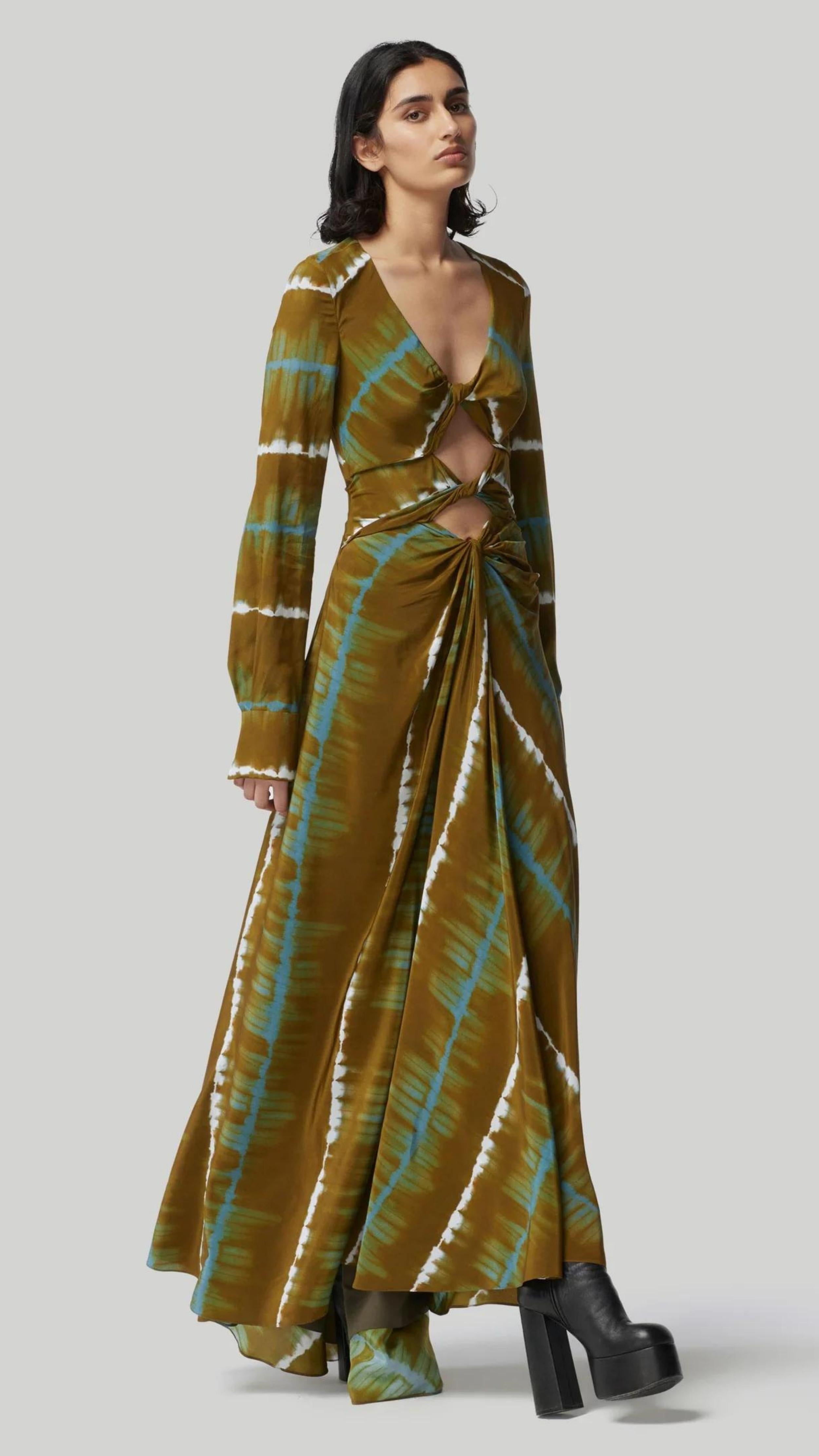 Altruzarra, Helenos Dress. 100% silk and shibori dyed in beautiful olive green and ecru pattern with a highlight pop of blue/green. It features a v neckline, long sleeves and a full skirt with front cut out and twist details. This pre-fall 2023 dress is shown on a model facing to the front and side. Available at experience 27 in madrid, spain.