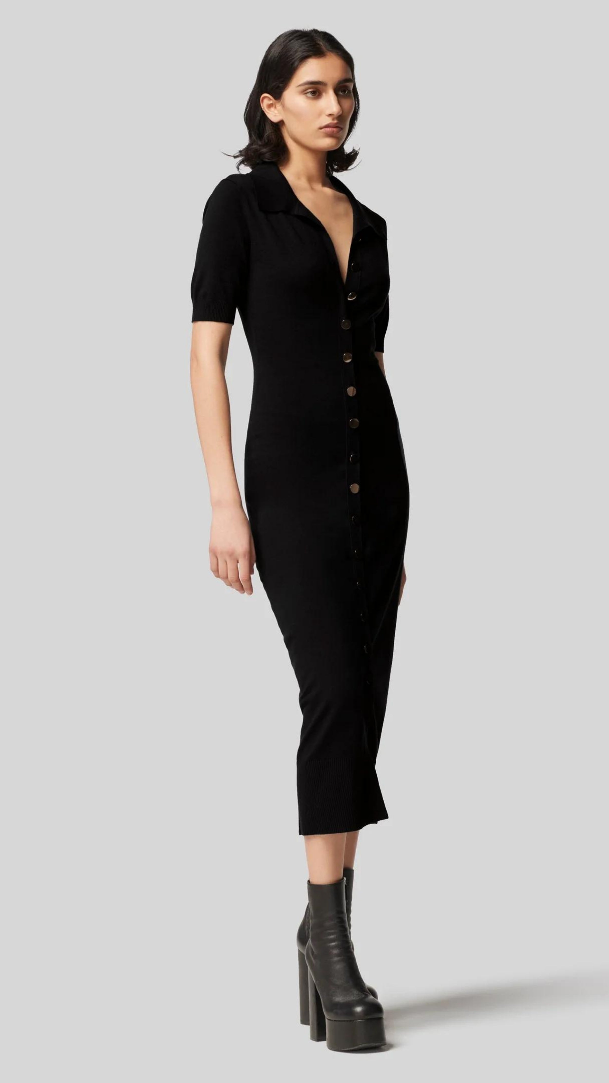 Altruzarra Hestia Dress in Black. A lightweight, super soft knit dress. Body fitting with gold buttons from front top to bottom. Midi length, shirt collar and half short sleeves. Black. Shown on model from front side view. Available at experience 27 in Madrid Spain.