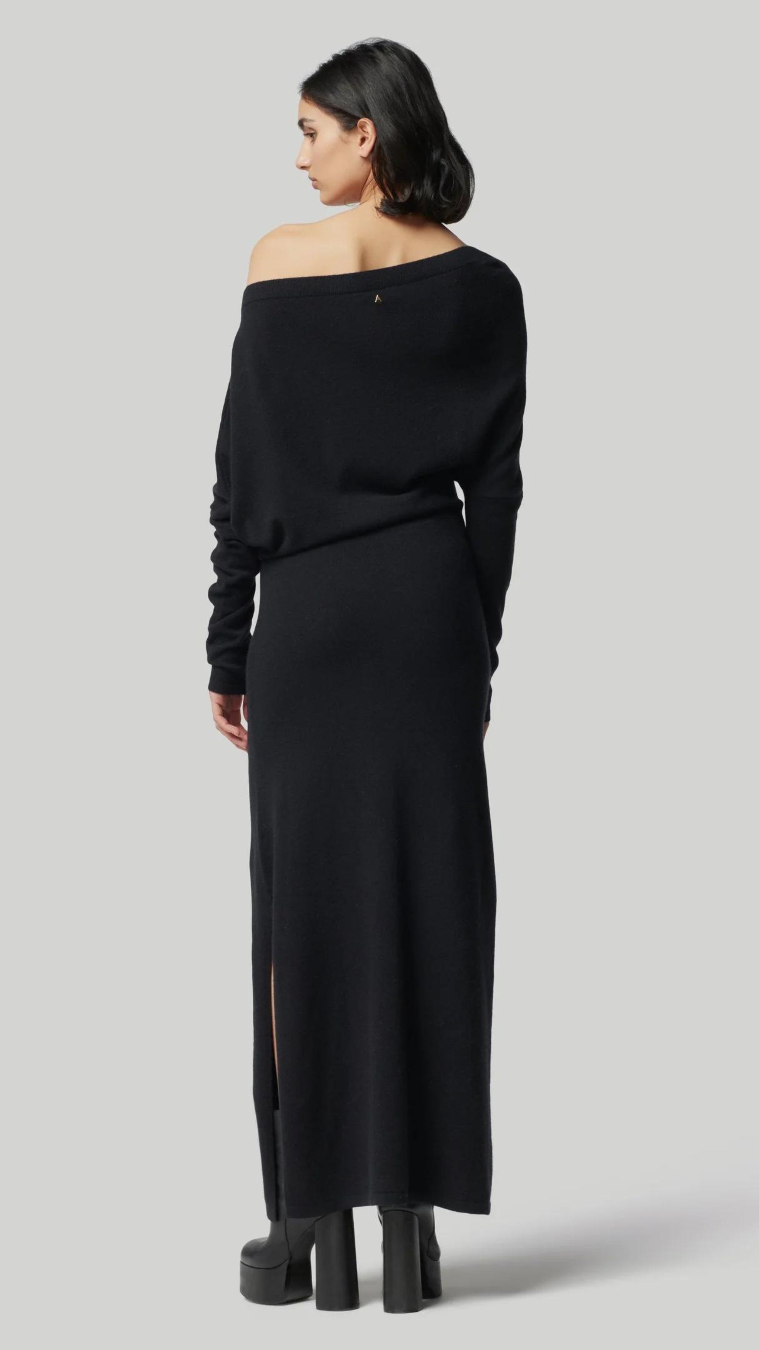 Altuzarra Black Cashmere Kasos Dress. The dress features an oversized off-the-shoulder top, slim long sleeves, an ankle-length skirt with a side slit hem. Off duty ballerina elegance in the style. Photo shows model wearing the dress facing back.
