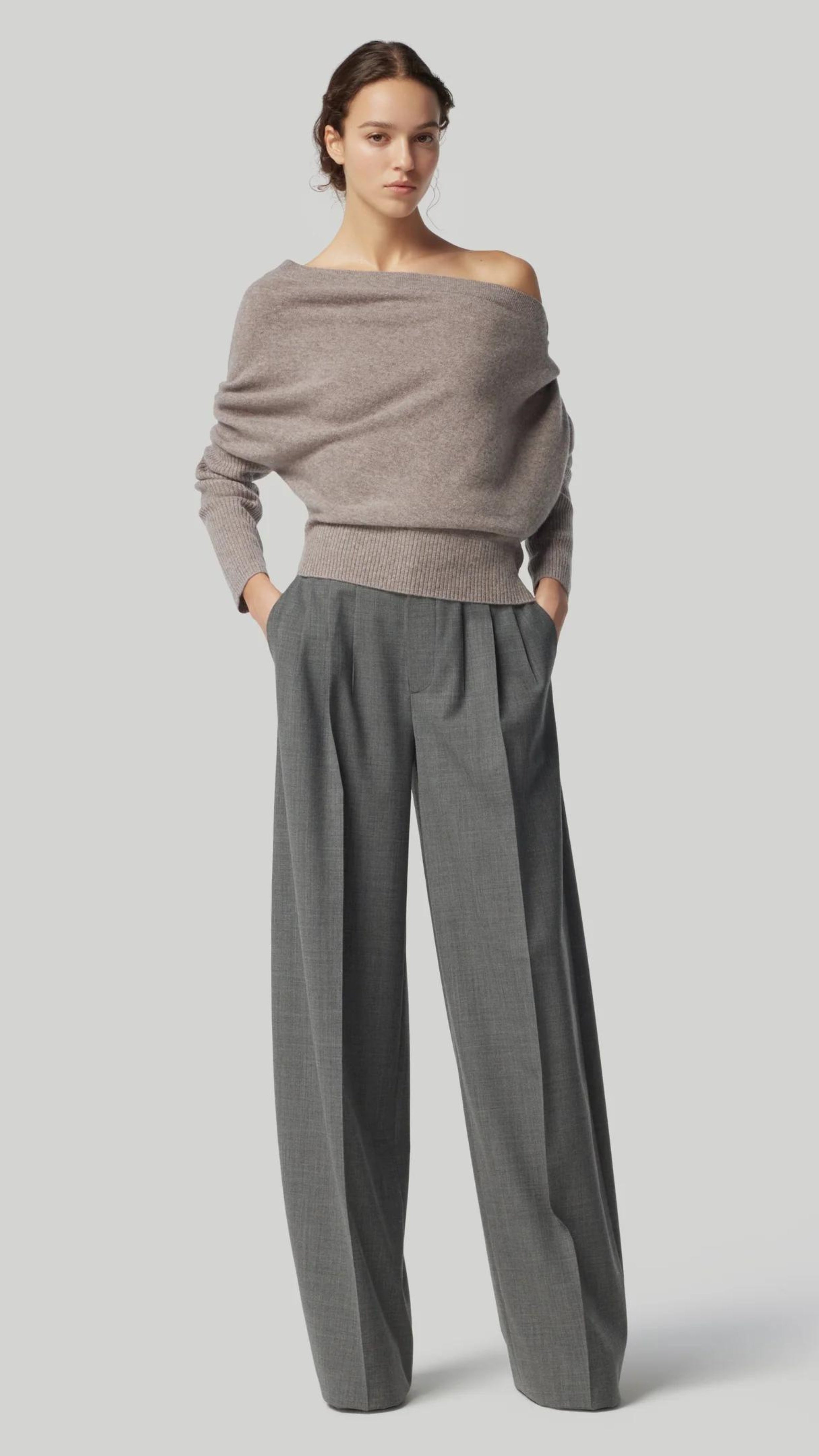 Altuzarra Paxi Cashmere Sweater in Grey. Luxury soft knit jumper in light gray, off the shoulder style. With a fitted waist line and sleeves for an elegantly casual look. Shown on model facing front.