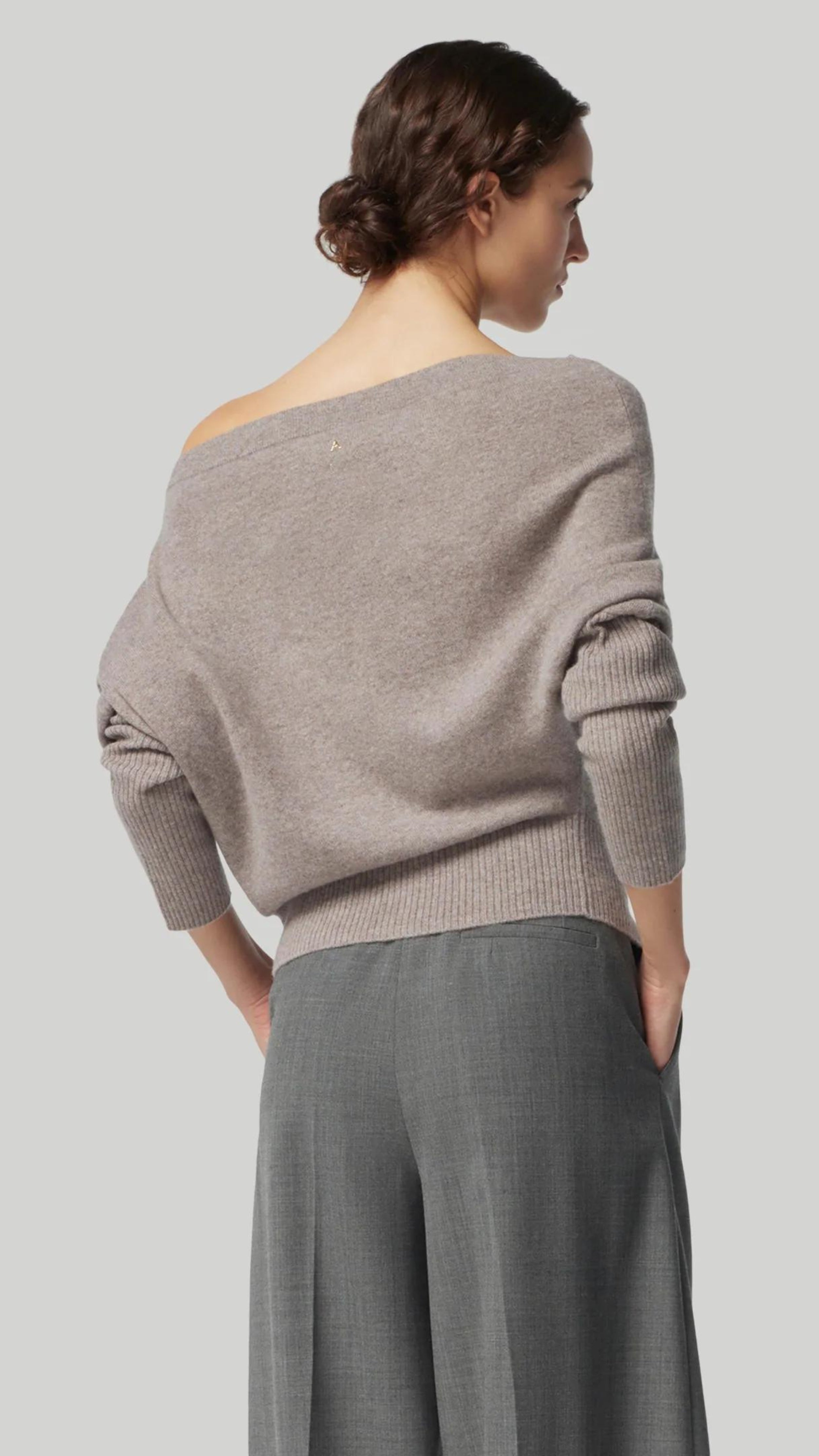Altuzarra Paxi Cashmere Sweater in Grey. Luxury soft knit jumper in light gray, off the shoulder style. With a fitted waist line and sleeves for an elegantly casual look. Shown on model facing to the back.