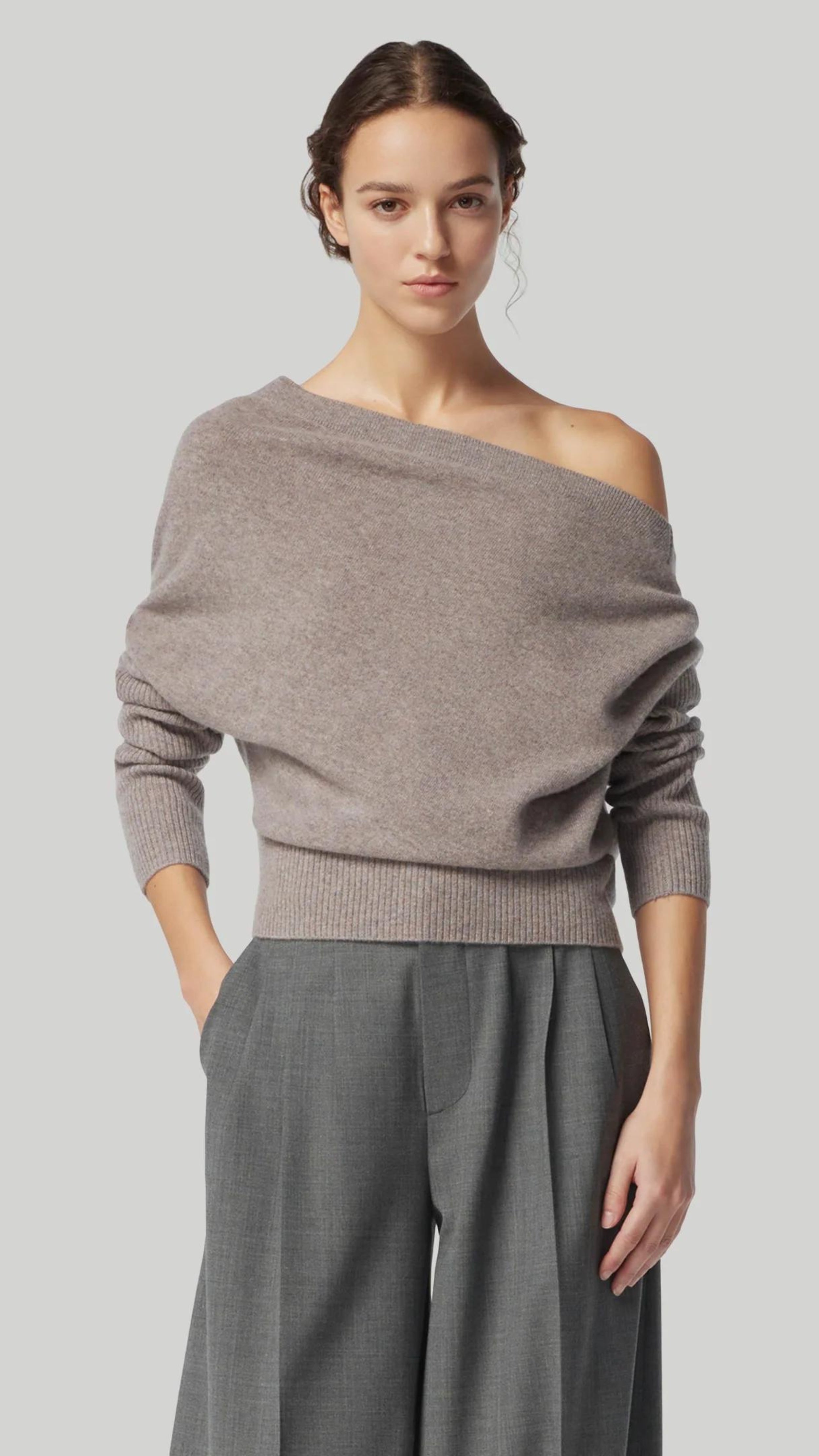 Altuzarra Paxi Cashmere Sweater in Grey. Luxury soft knit jumper in light gray, off the shoulder style. With a fitted waist line and sleeves for an elegantly casual look. Shown on model facing front 