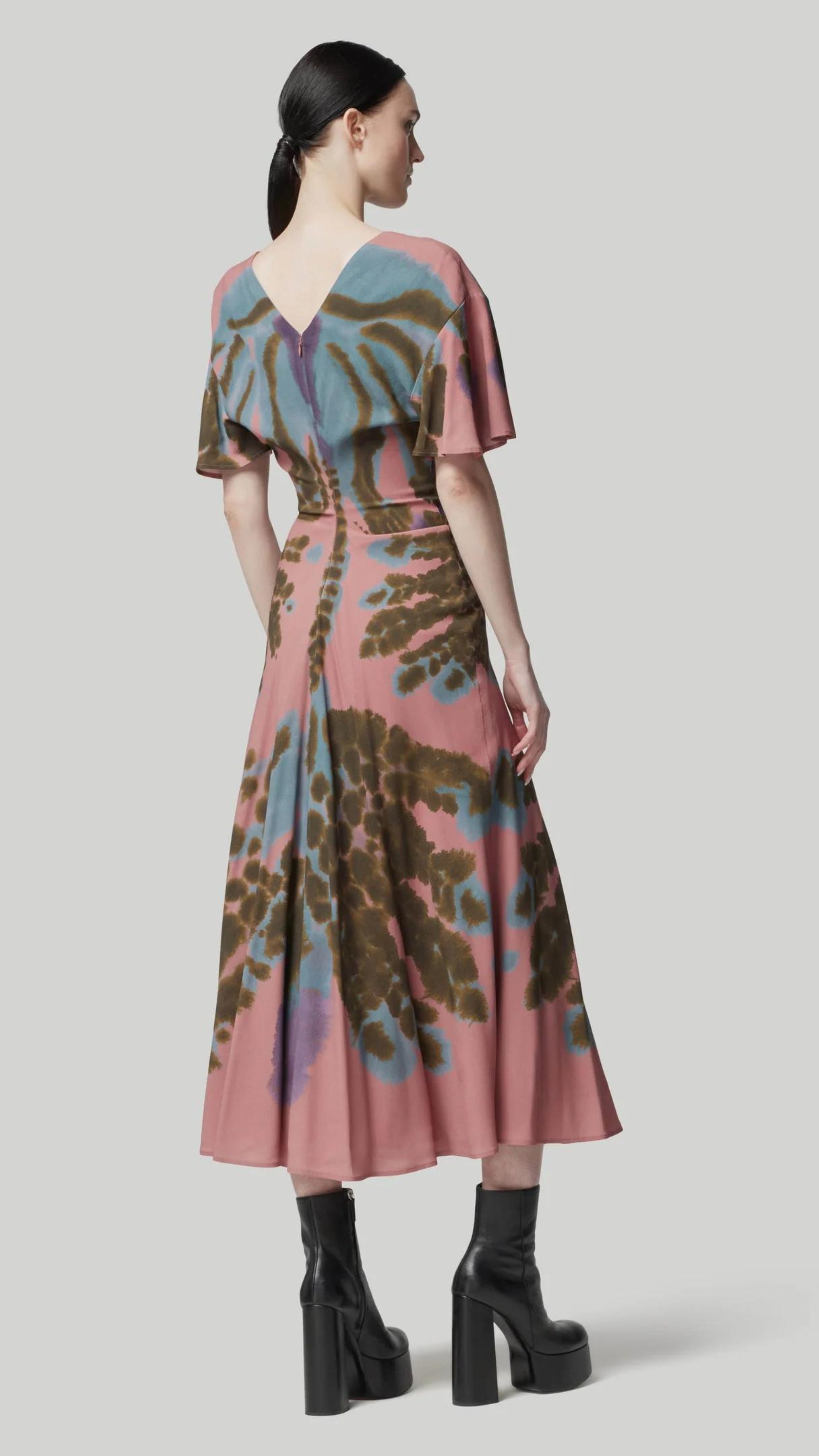Altuzarra Pelopenese Dress. Rose pink, sky blue and green rorschach pattern midi dress. With a v neckline and soft draping half sleeves. Flowing skirt with waist line rouching. Shown on model facing to the back.