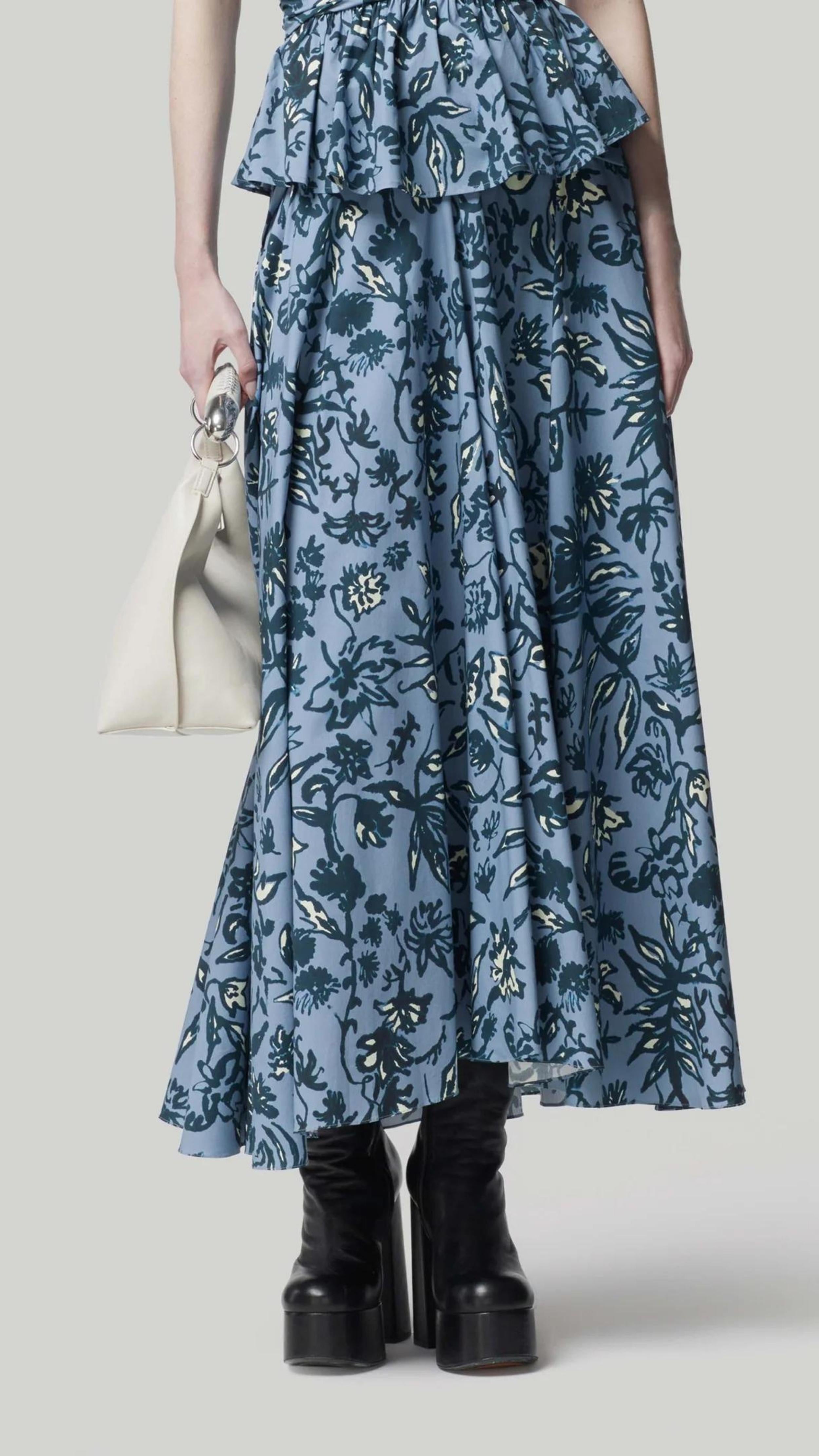 Altuzarra Pythia Skirt in Amsonia Shibori Flower. A midi length, aline style skirt with beautiful twist detail at the waist. Crafted in 100% cotton with a natural ecru color floral print over a light blue background. Shown on model facing front. Available at experience 27 in Madrid spain.