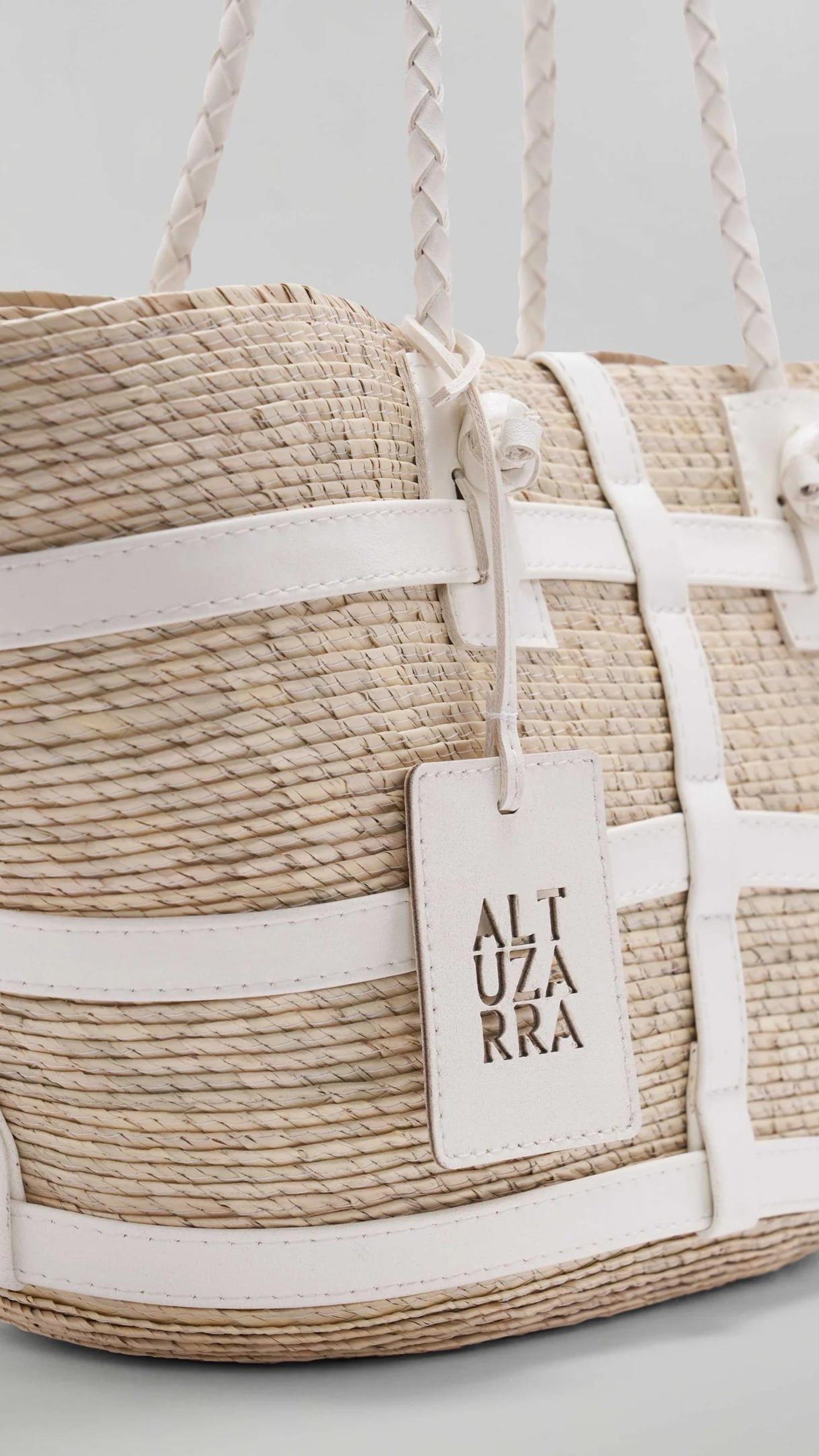 Altuzara Watermill Bag Small in White. Crafted in Mexico from natural palm fibers and detailed with soft white leather. The hand straps are braided leather and it comes with a laser cut detailed Altuzarra hang tag. This photo shows a close up of the details.