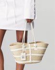Altuzara Watermill Bag Small in White. Crafted in Mexico from natural palm fibers and detailed with soft white leather. The hand straps are braided leather and it comes with a laser cut detailed Altuzarra hang tag. This photo shows the bag being held by the model.