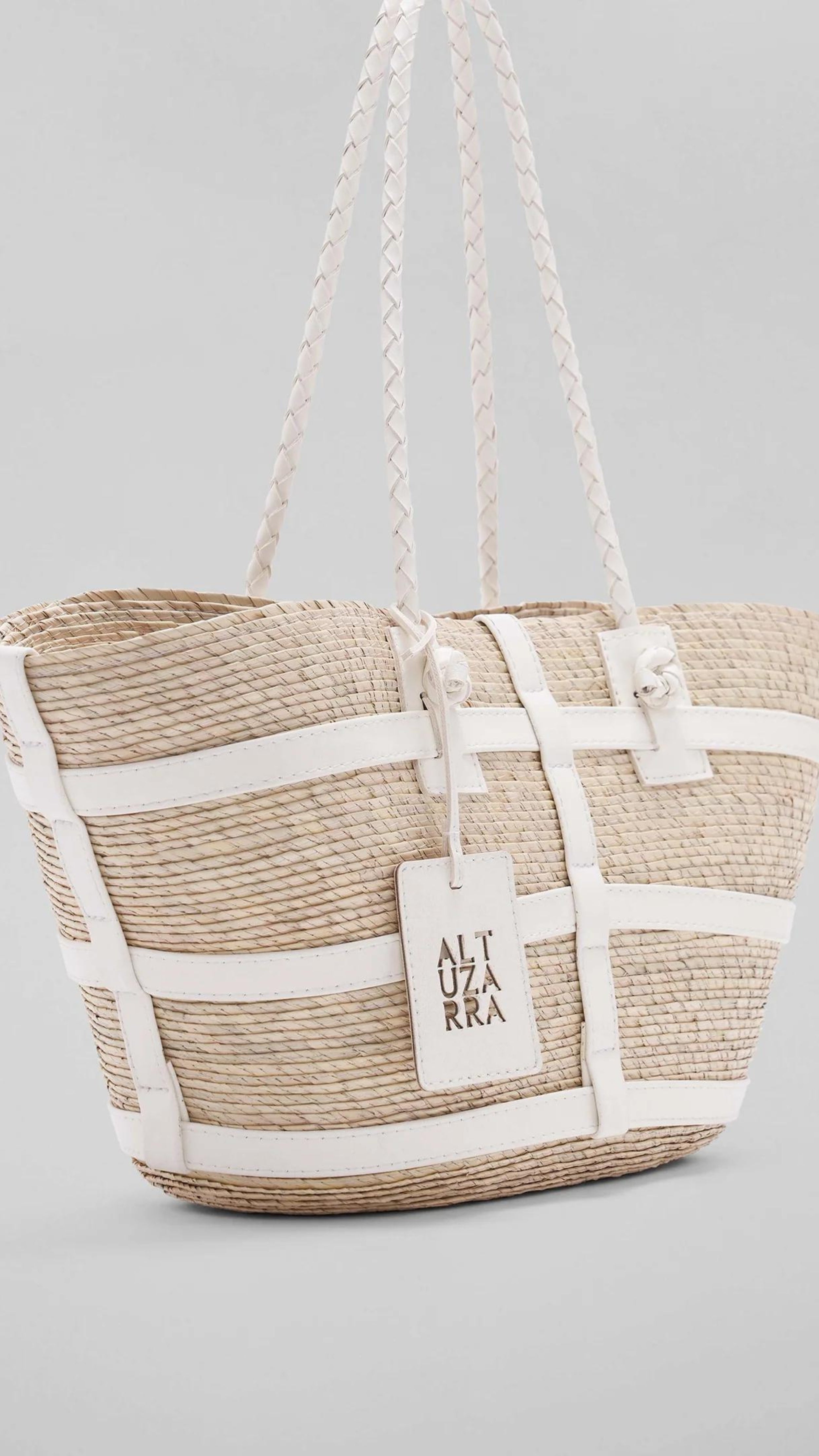 Altuzara Watermill Bag Small in White. Crafted in Mexico from natural palm fibers and detailed with soft white leather. The hand straps are braided leather and it comes with a laser cut detailed Altuzarra hang tag. This photo shows the full bag bag from a slight angle.