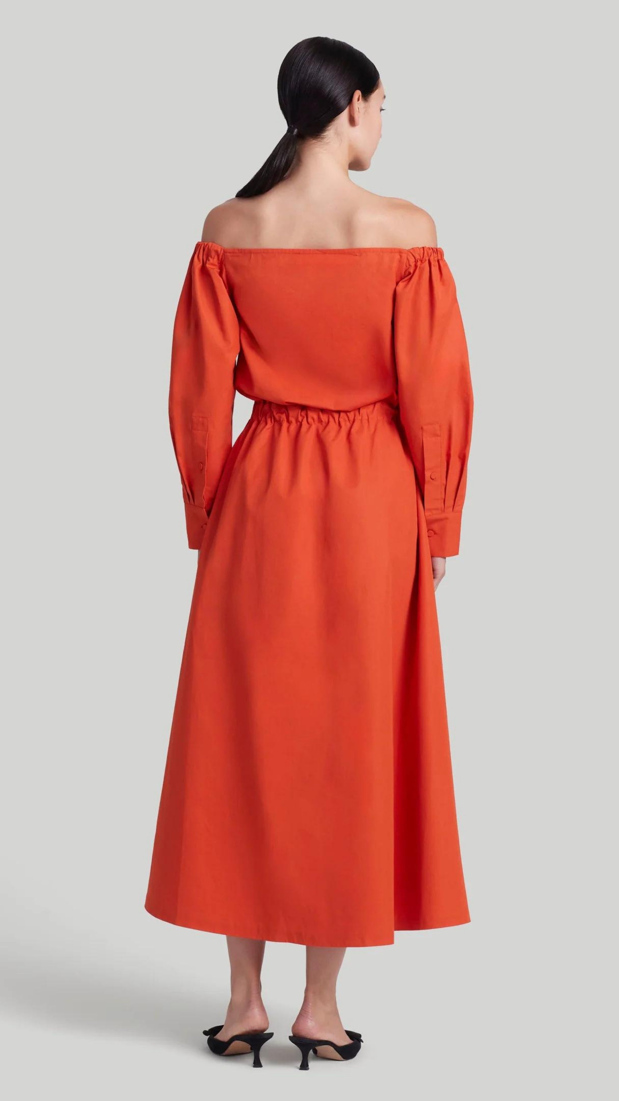 Altuzarra Zora dress shirt dress style soft cotton midi dress in red orange color. Made in Italy. The dress has off the shoulder neckline, puff sleeves and an elasticated waist waistband. Shown on model facing back