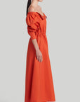 Altuzarra Zora dress shirt dress style soft cotton midi dress in red orange color. Made in Italy. The dress has off the shoulder neckline, puff sleeves and an elasticated waist waistband. Shown on model facing side