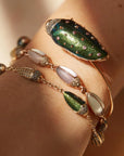 Bibi van der Velden Mini Scarab Eternity Bracelet. Made in 18k rose gold, this bracelet has nine  scarab beetles, each made with translucent, matte gemstones in soft shades. The beetles' heads are paved with pale brown diamonds. Shown being worn on an arm.