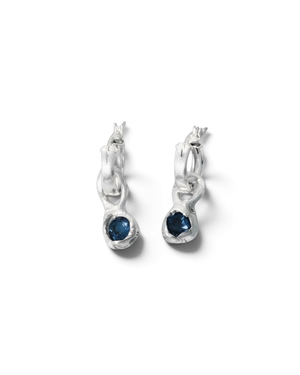 Sterling silver hoop earrings with blue topaz drops resting on beige textured surface, close-up