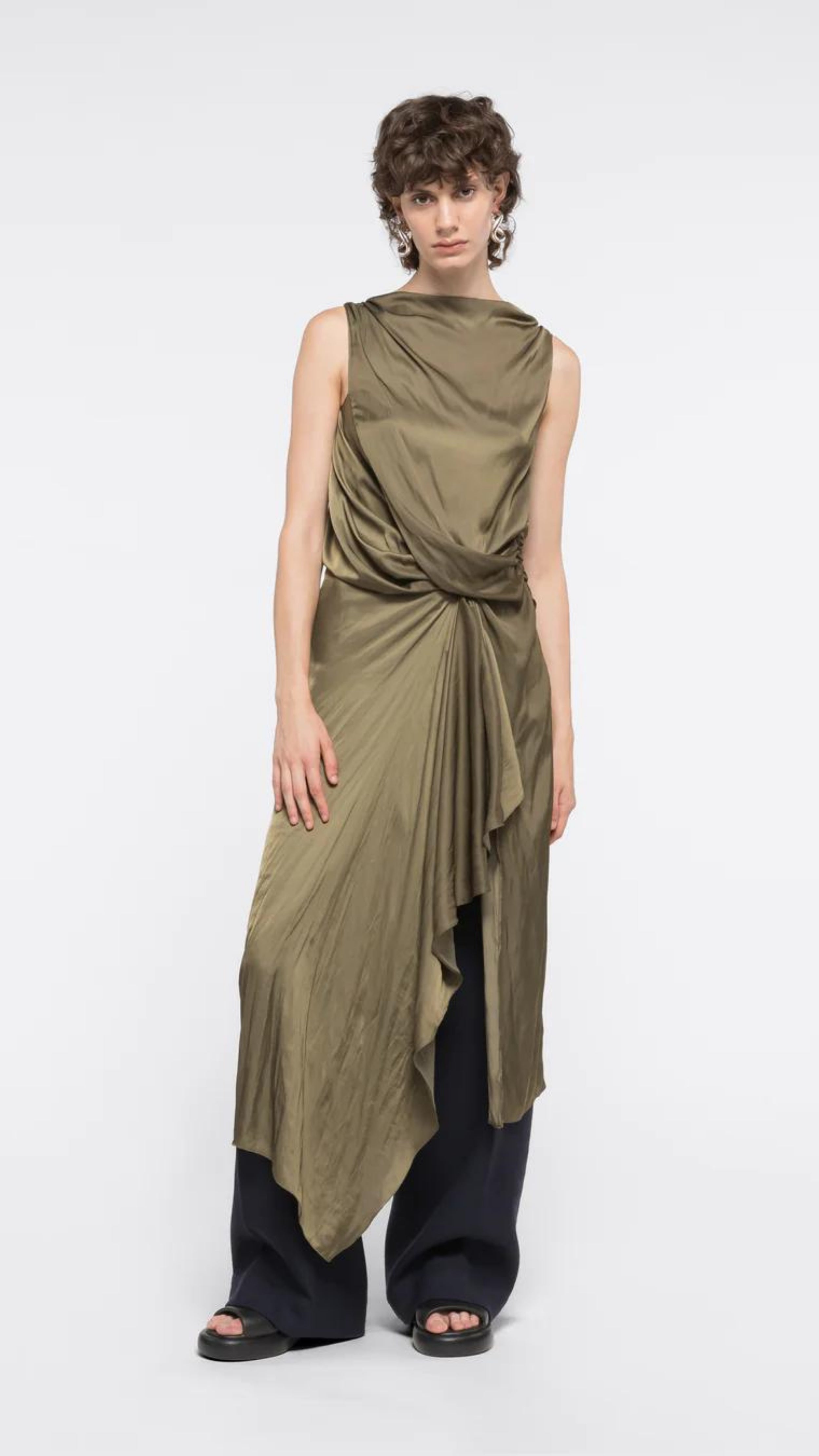 AZ Factory Colville Molly Molloy Lucinda Chambers, Sleeveless Draped Dress in Khaki An elegant olive green formal dress with a silhouette defined by a straight neckline and asymmetrical hemline. The waistline has detailed draping and the front leg as a slit. Shown on model facing front.