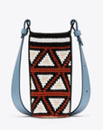 AZ Factory Colville Molly Molloy Lucinda Chambers, The Little Guy Bag A mini cylinder bag is crafted in Wayuu Colombia and completed with fine Italian leather details. It has a burgundy, ecru and black pattern for the purse body and a sky blue adjustable leather strap. Front view.