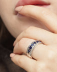 Conde de diamante Azura Ring. 18K white gold band ring with a center row of carré cut blue sapphires flanked on each side by bands of pave white diamonds. Shown on model facing front.