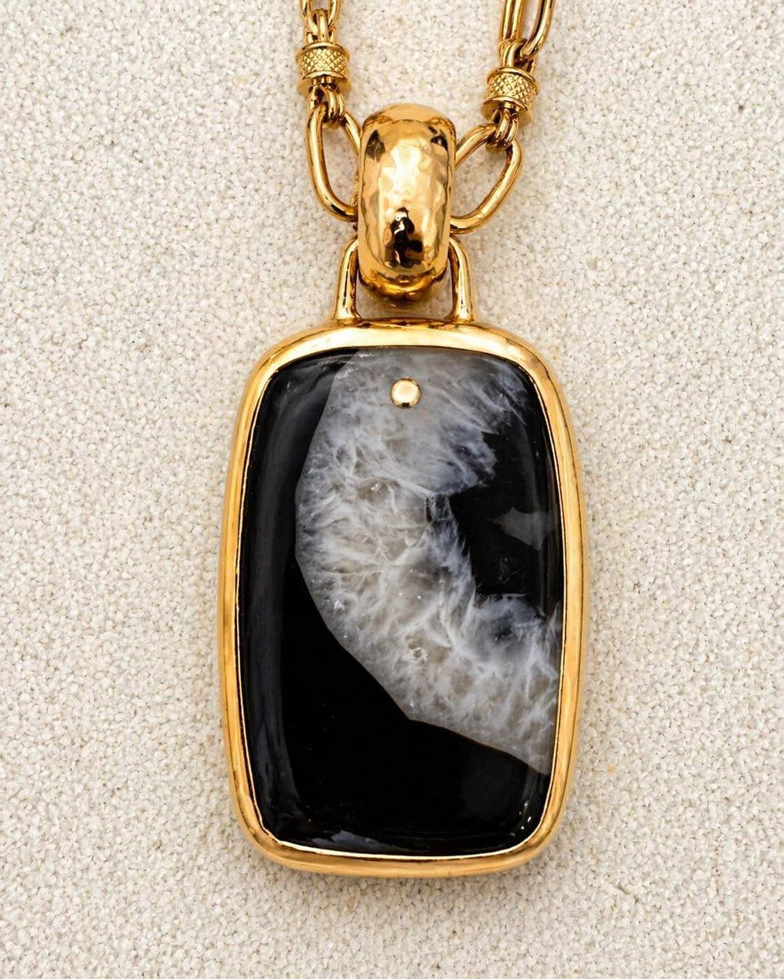 Aura Pendant close-up showing black and white mineral glass stone in hammered gold bezel with polished bale