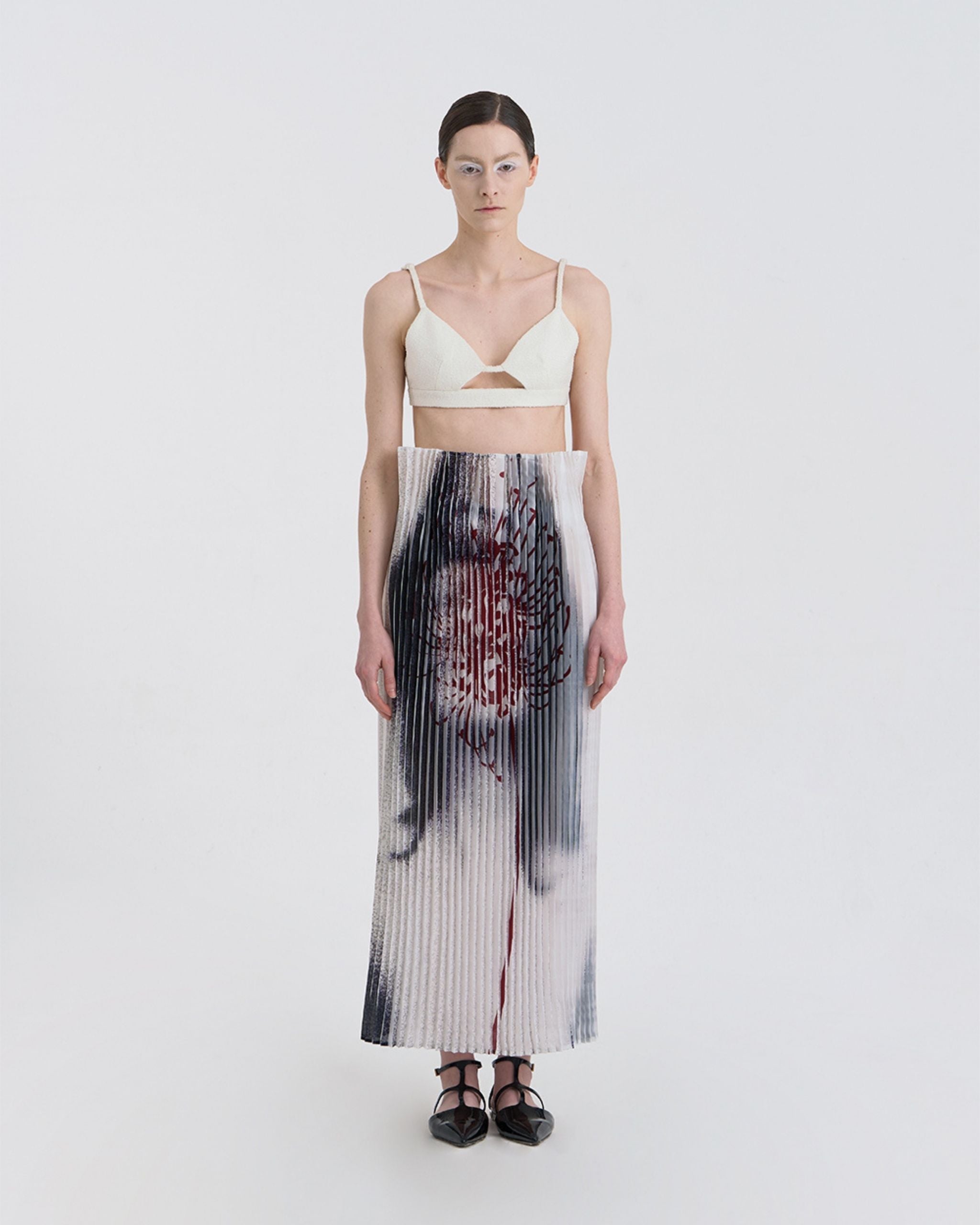 Front view of JINSUN Anamo Pleated Skirt in printed pleated fabric with blurred digital motif.