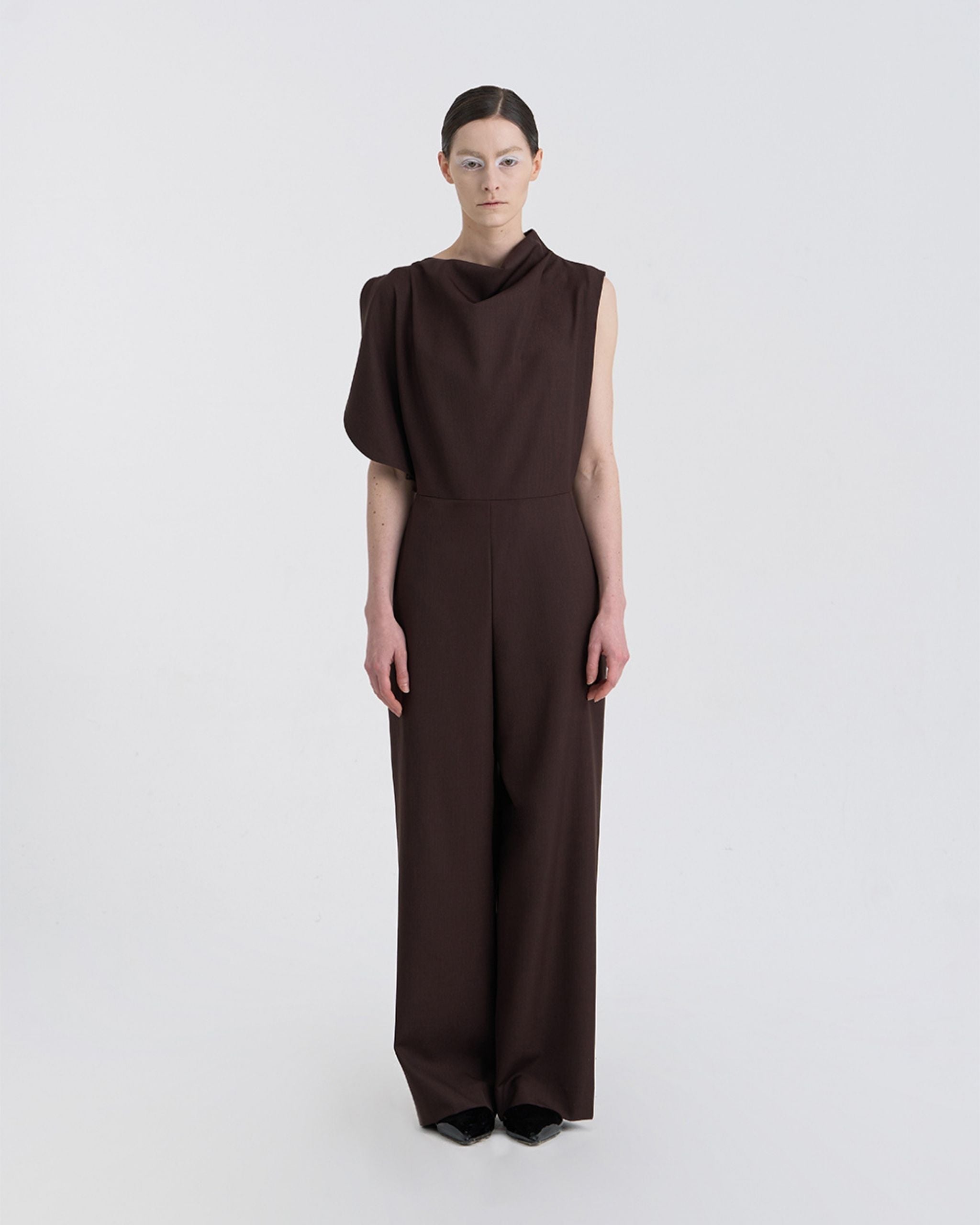 Front view of model wearing JINSUN Filante Wool Jumpsuit in brown with asymmetric draped shoulder